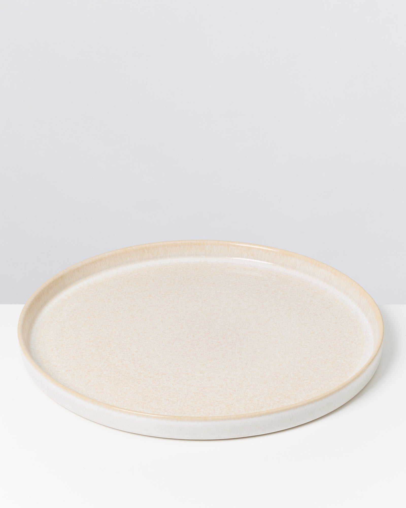 Beiger, runder Keramikteller auf einem weißen Hintergrund.