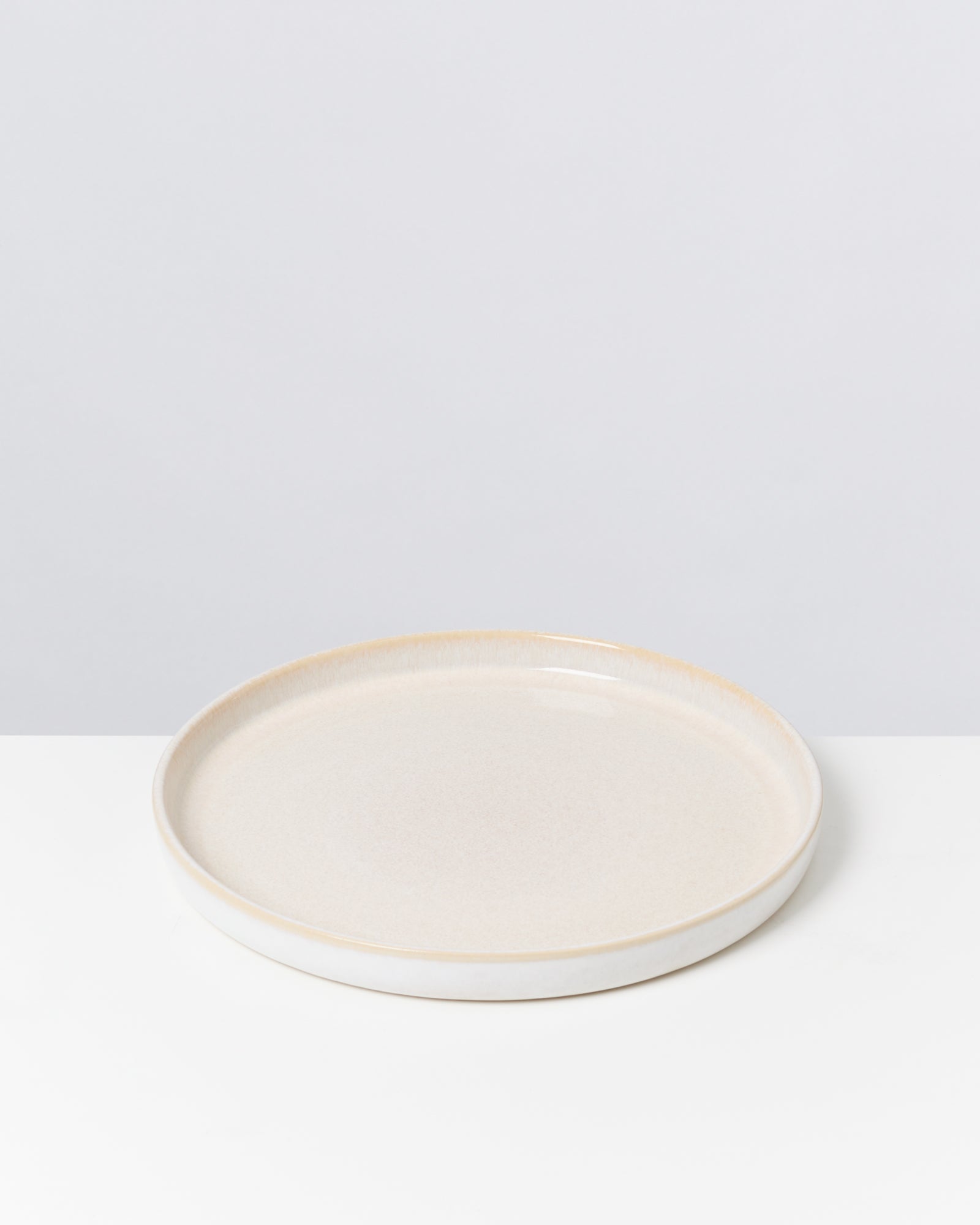 Beiger, runder Keramikteller auf weißem Hintergrund.