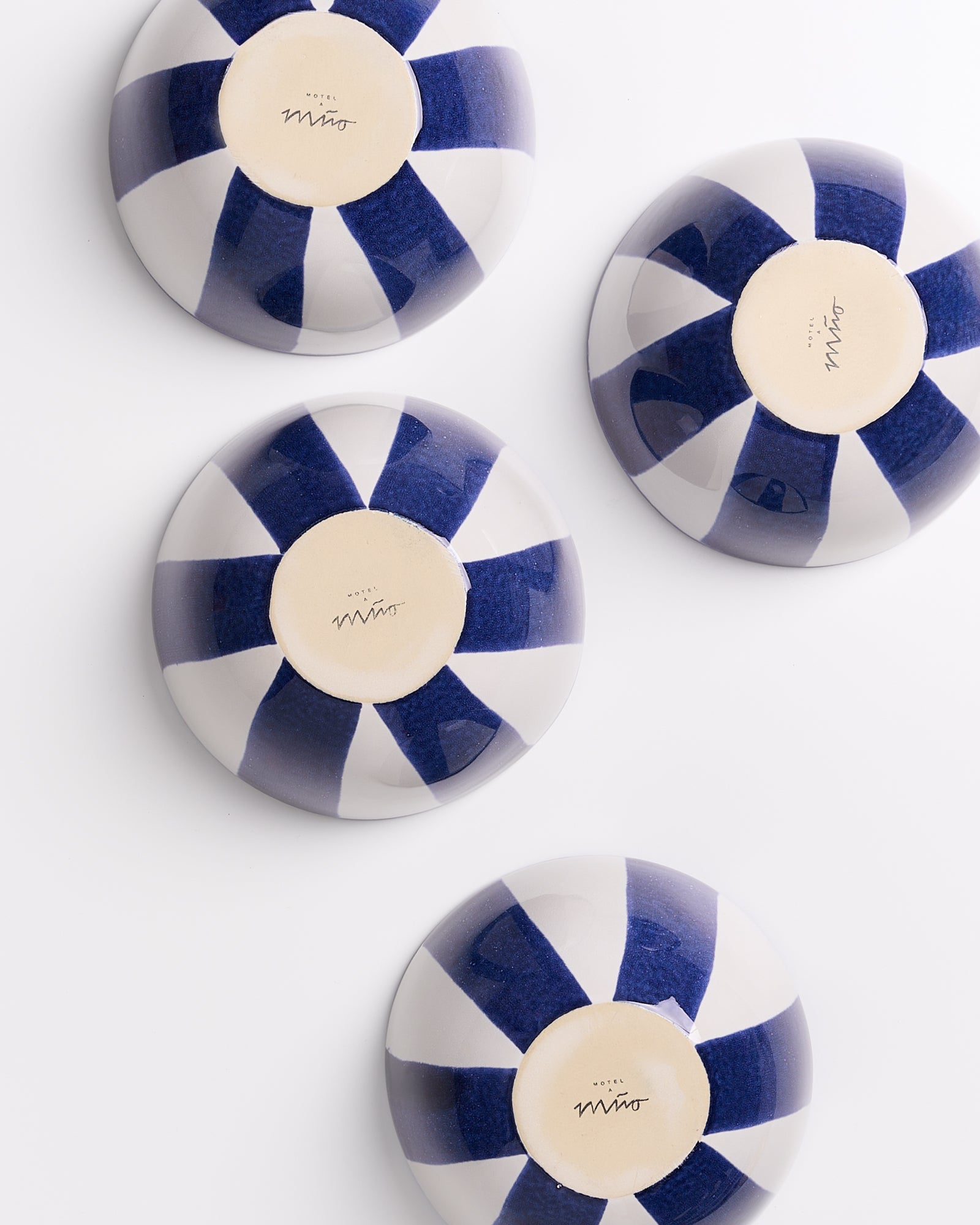 Vier umgedrehte, gestreifte Keramikteller in Blau und Weiß auf einer weißen Oberfläche.