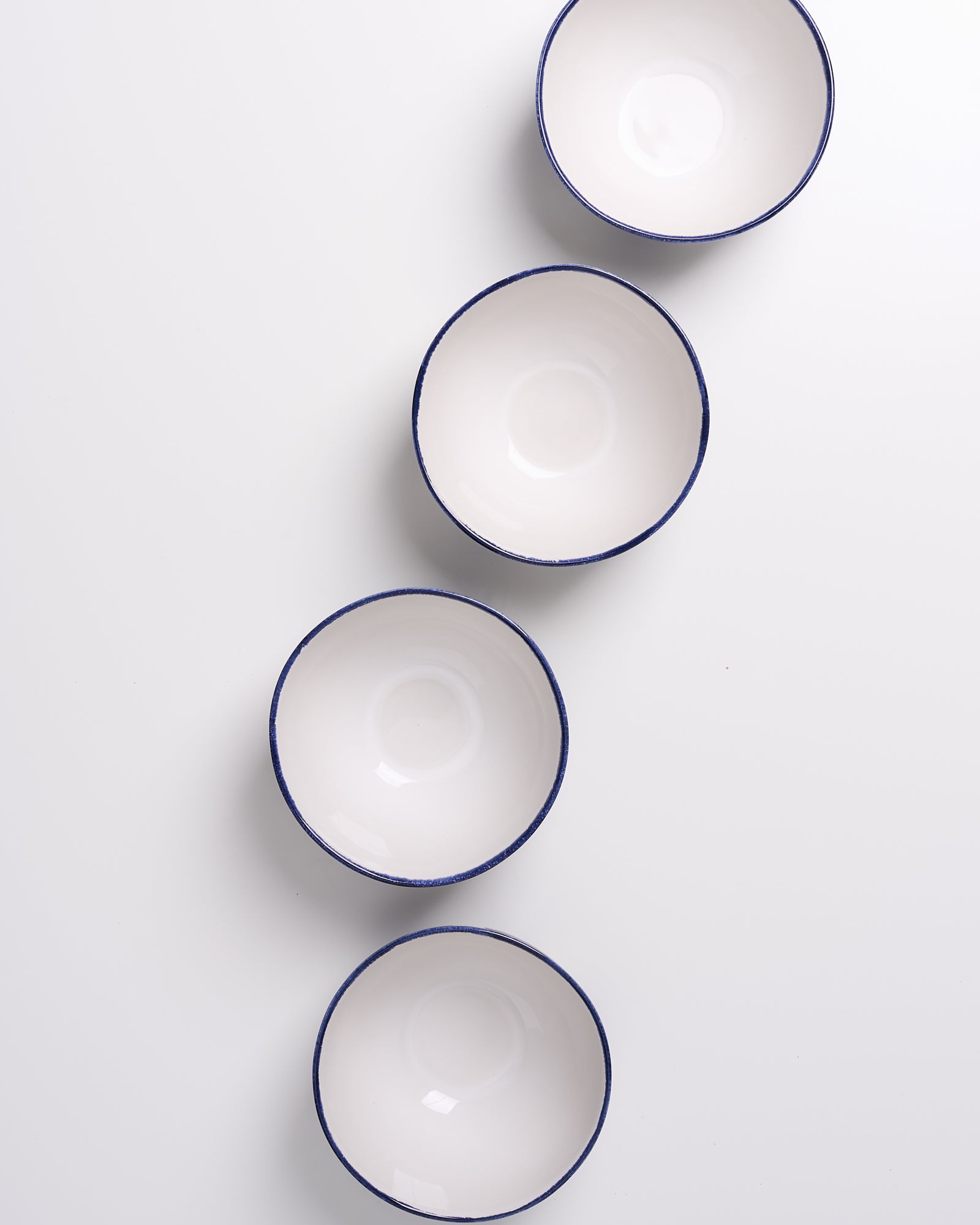 Vier weiß-blaue Schüsseln in einer diagonalen Reihe auf einem weißen Hintergrund.