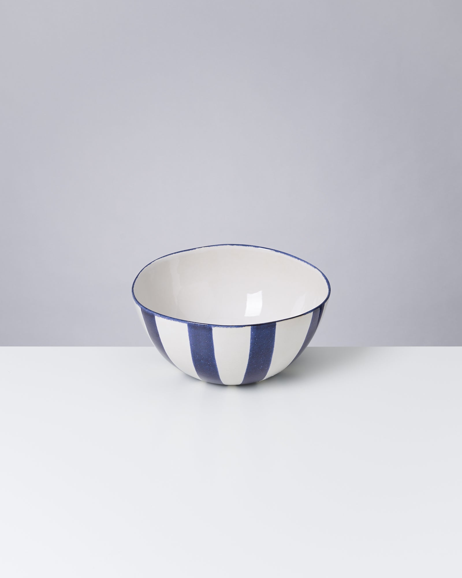 Weiße Keramikschale mit blauen Streifen steht auf einem weißen Tisch vor grauem Hintergrund.