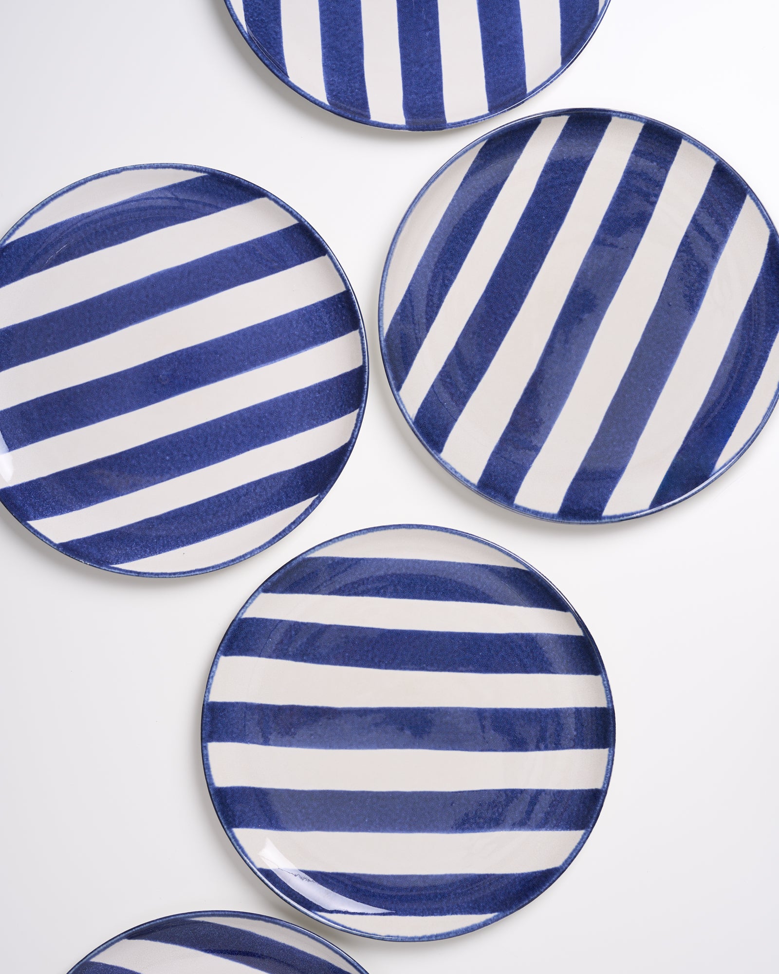 Fünf runde Teller mit diagonalen blauen und weißen Streifen auf weißem Hintergrund.