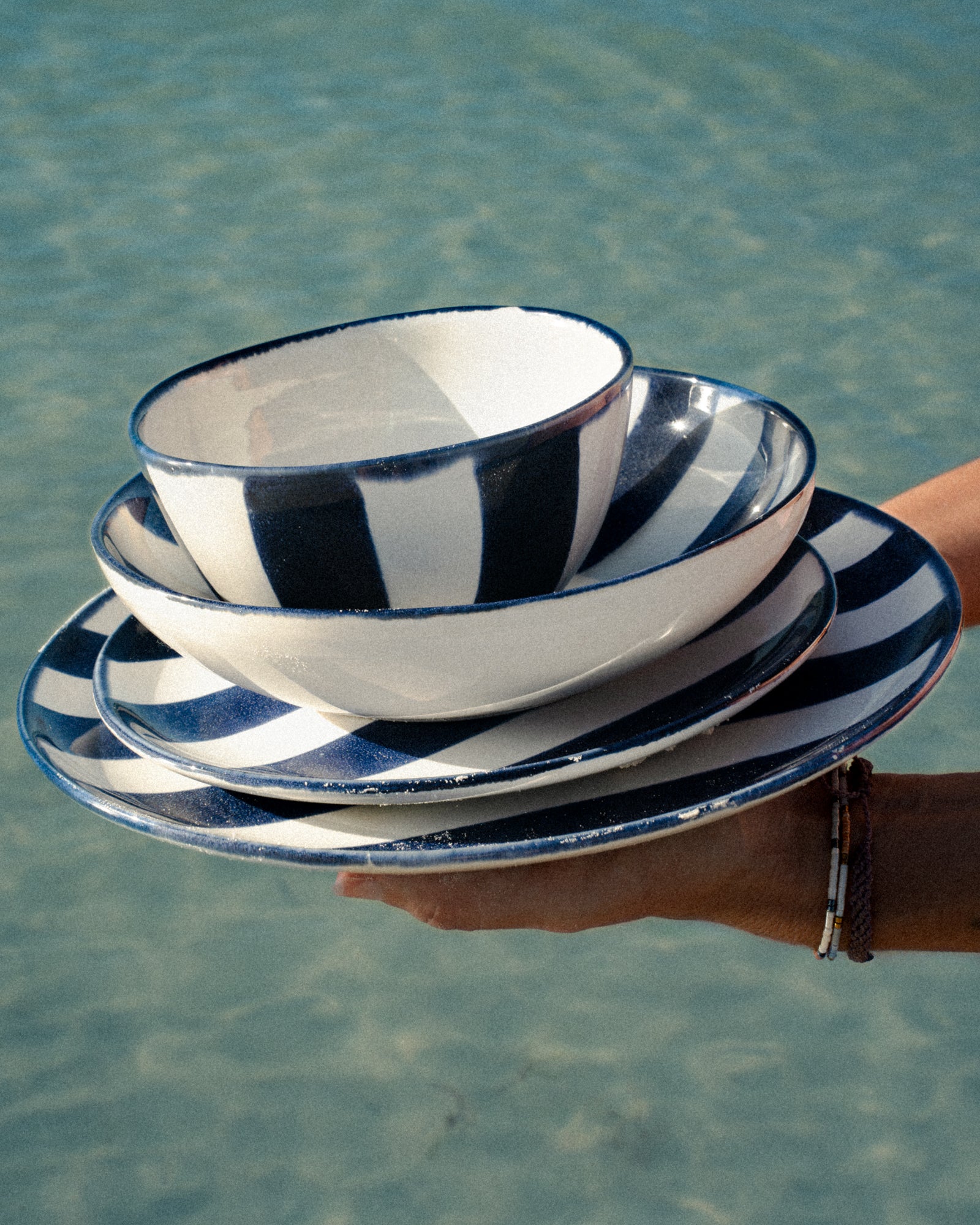 Eine Person hält gestreifte, schwarz-weiße Schalen und Teller vor einem Hintergrund aus Wasser.
