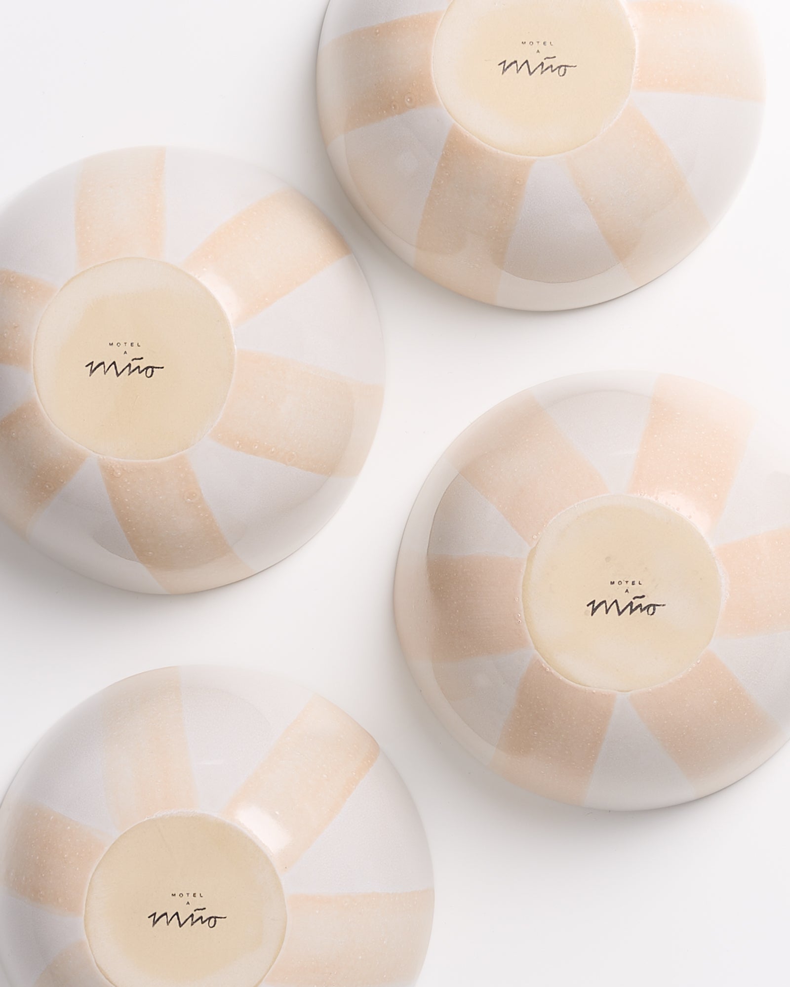 Vier umgedrehte Teller mit weißen und cremefarbenen Streifen auf der Unterseite, auf einem weißen Hintergrund.