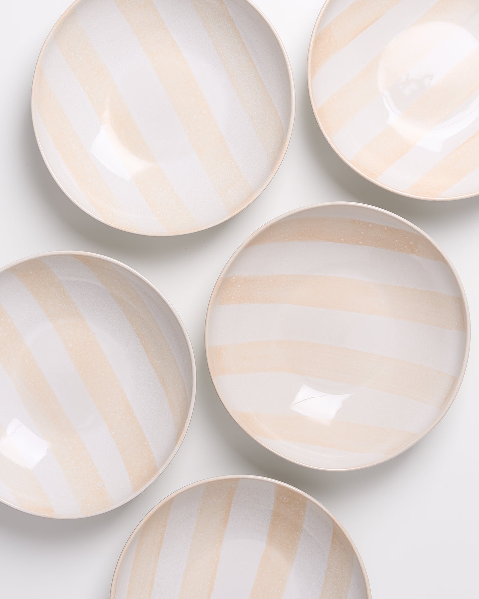 Fünf weiß-beige gestreifte Schalen liegen auf einer weißen Oberfläche.