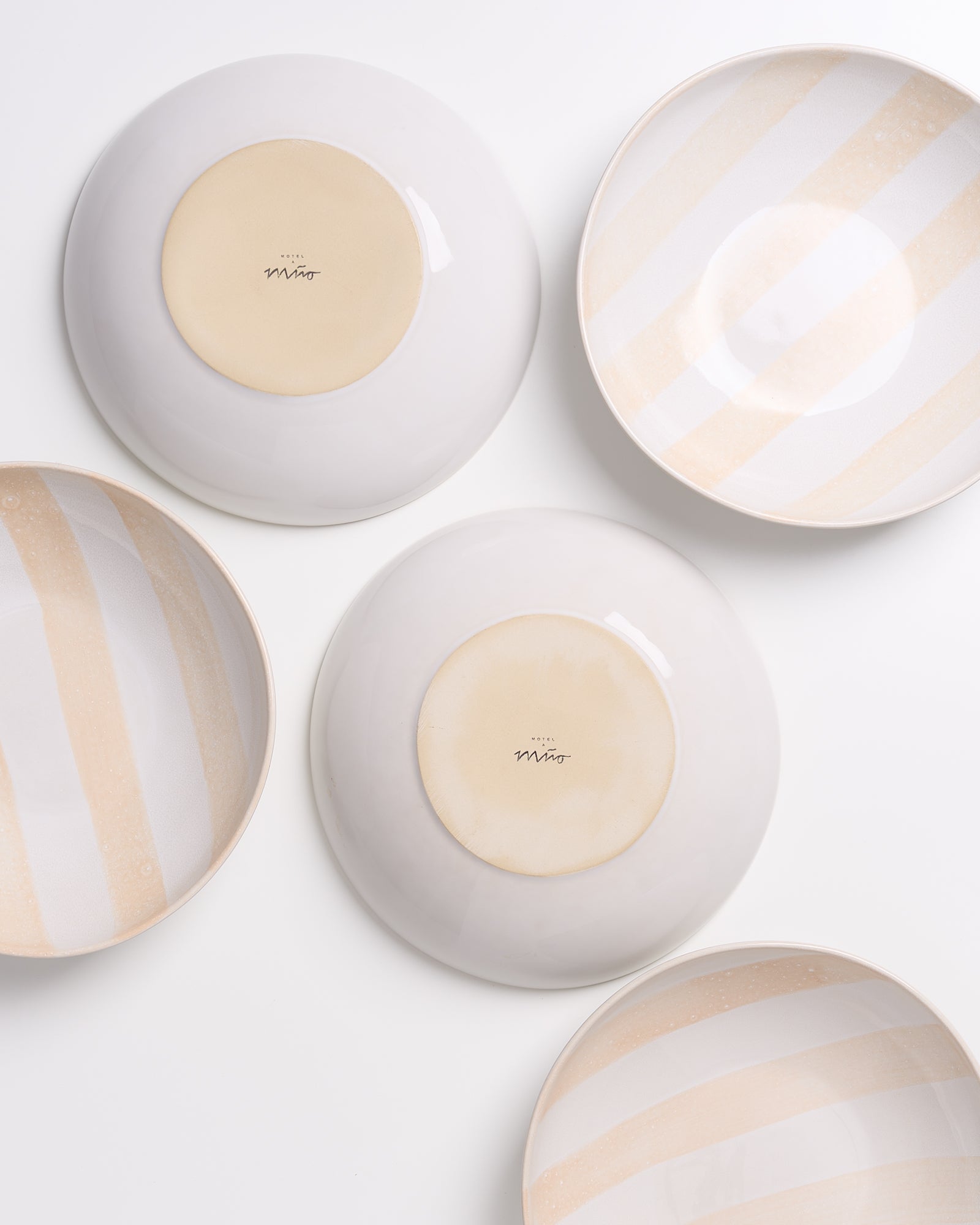 Fünf Keramikteller, einige mit beigen Streifenmustern, liegen teils umgedreht auf einer weißen Oberfläche.