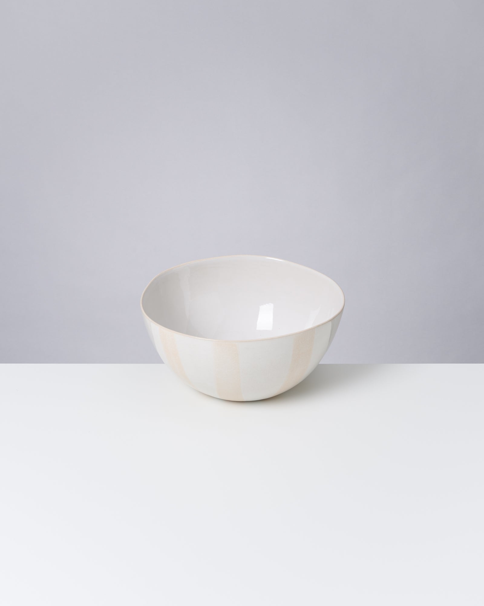Weiße, glatte Schüssel auf einem weißen Tisch vor grauem Hintergrund.
