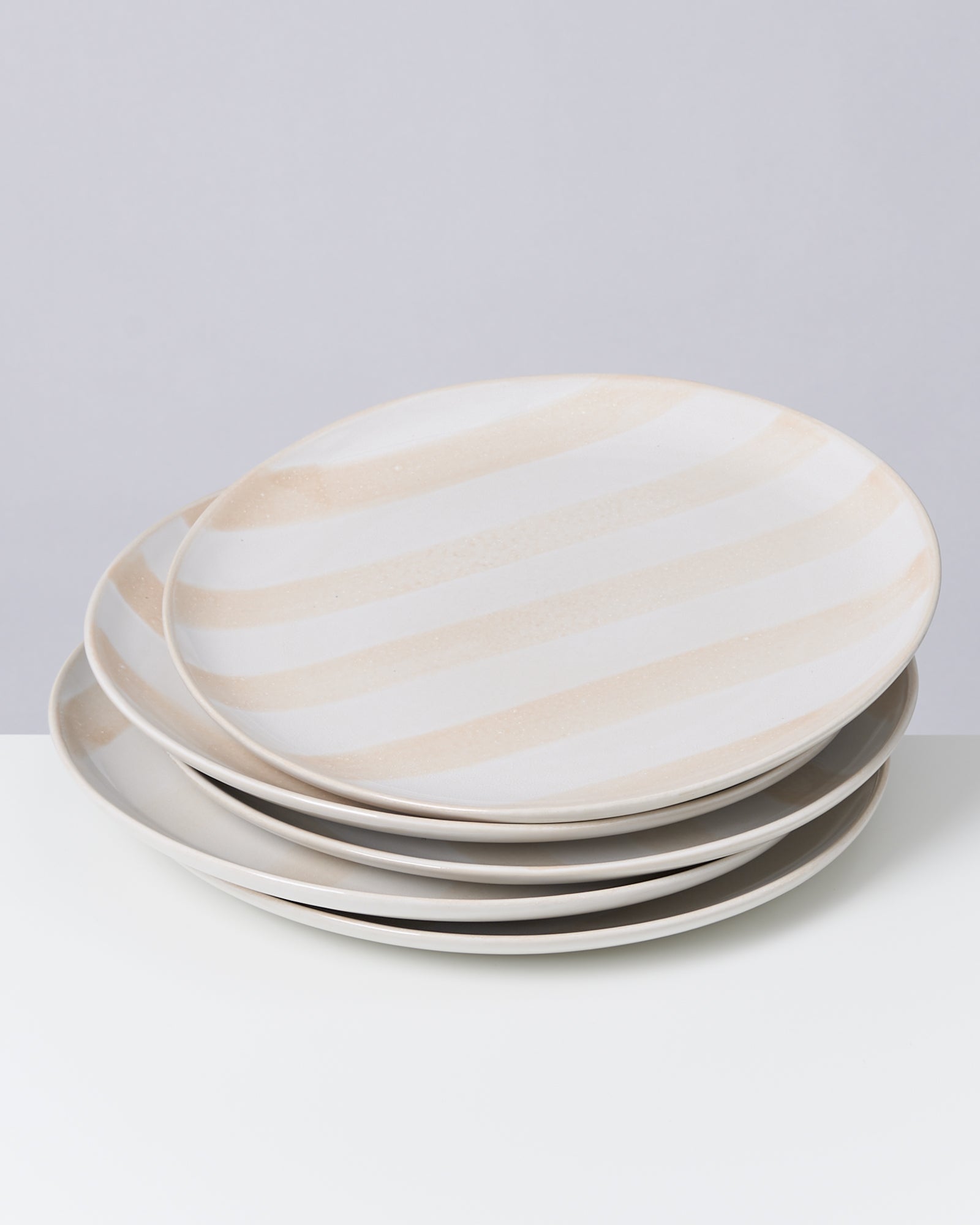 Vier gestreifte Teller in Pastellfarben aufeinander gestapelt auf einem weißen Tisch.