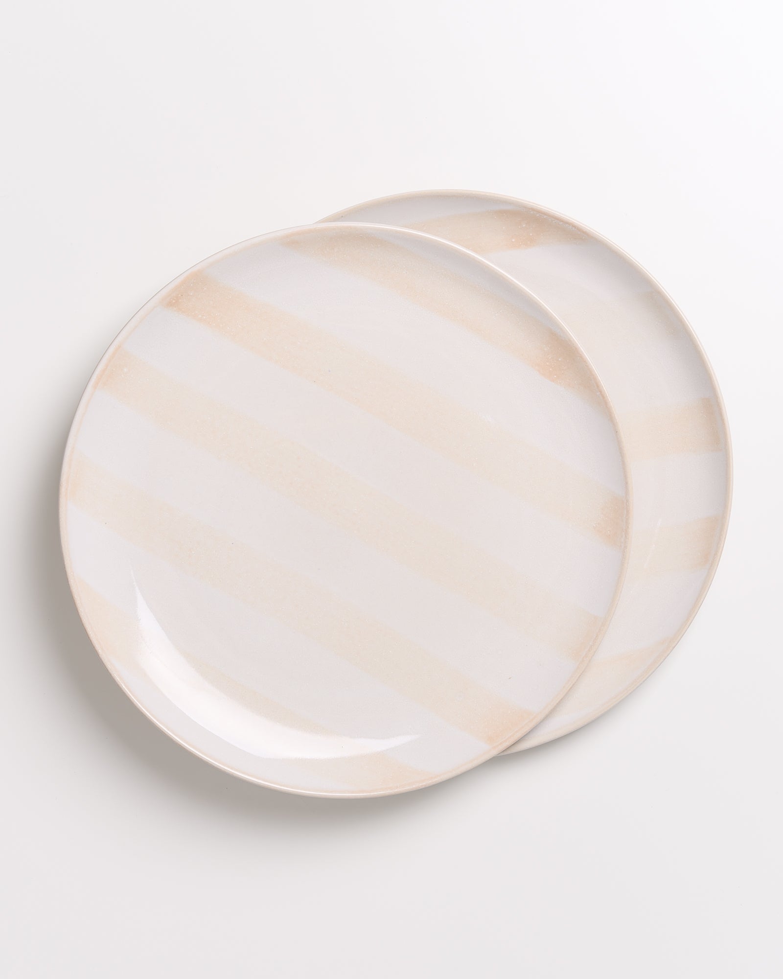 Zwei übereinanderliegende Teller mit dezentem, beigem Streifenmuster auf weißem Hintergrund.