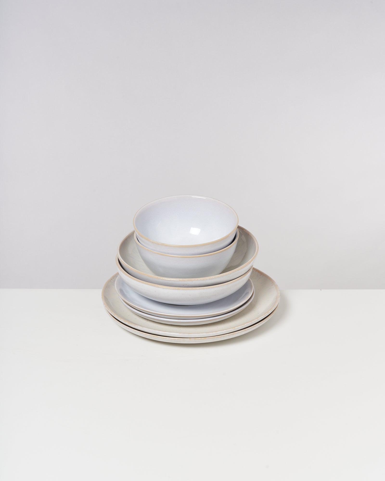 Gestapelte weiße Keramikschalen und Teller auf einem Tisch vor neutralem Hintergrund.