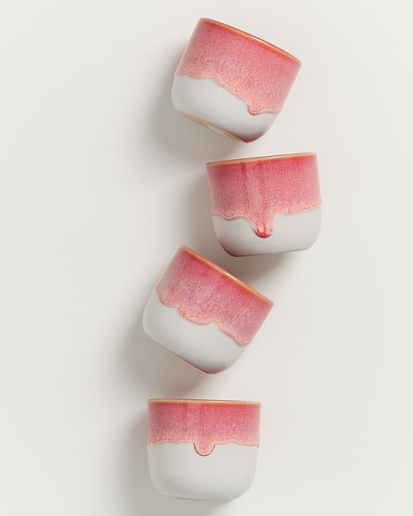 Vier rosa-weiße Keramiktassen sind diagonal auf einem weißen Hintergrund angeordnet.