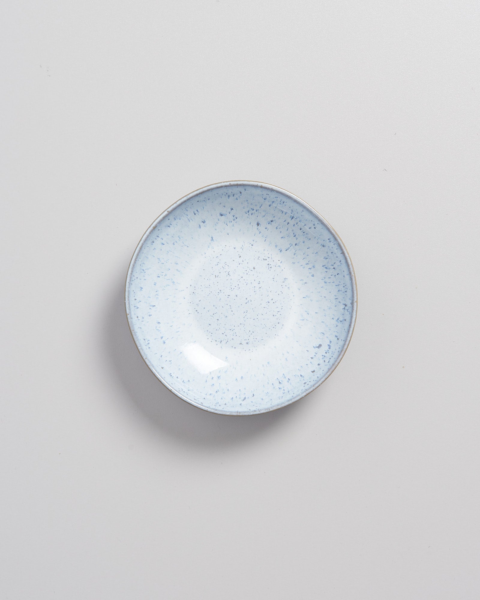 Kleiner, heller Teller mit blauen Sprenkeln auf einem hellgrauen Hintergrund.
