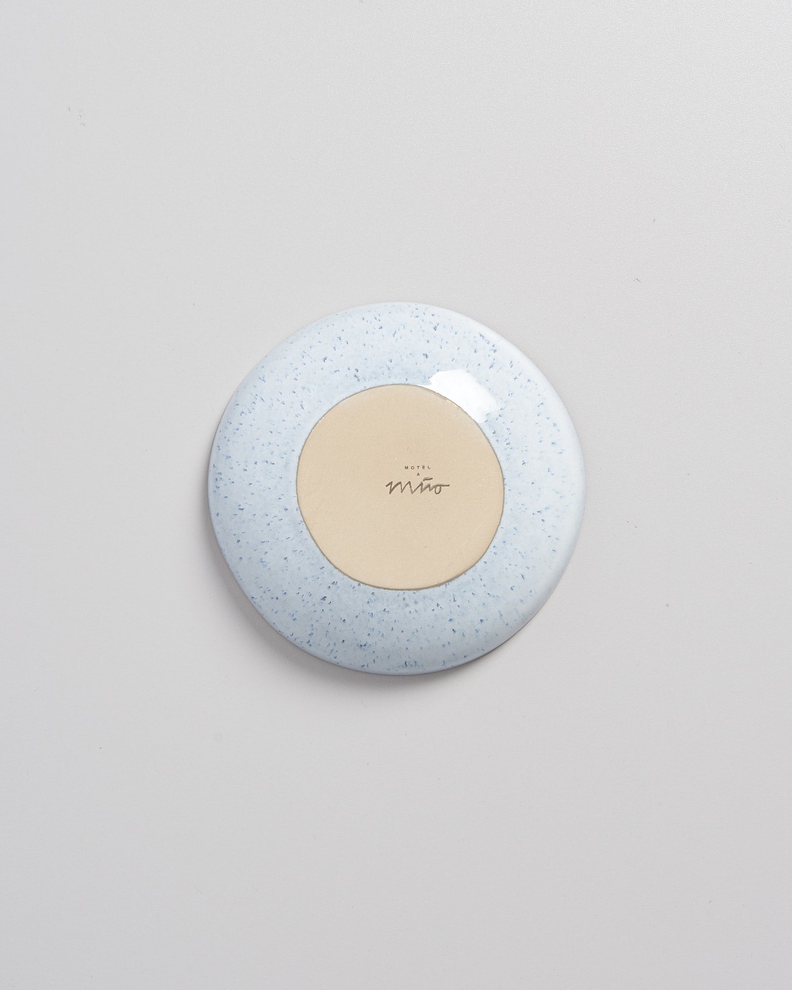 Runde hellblaue Scheibe auf grauem Hintergrund mit beiger Mitte und schwarzer Aufschrift.