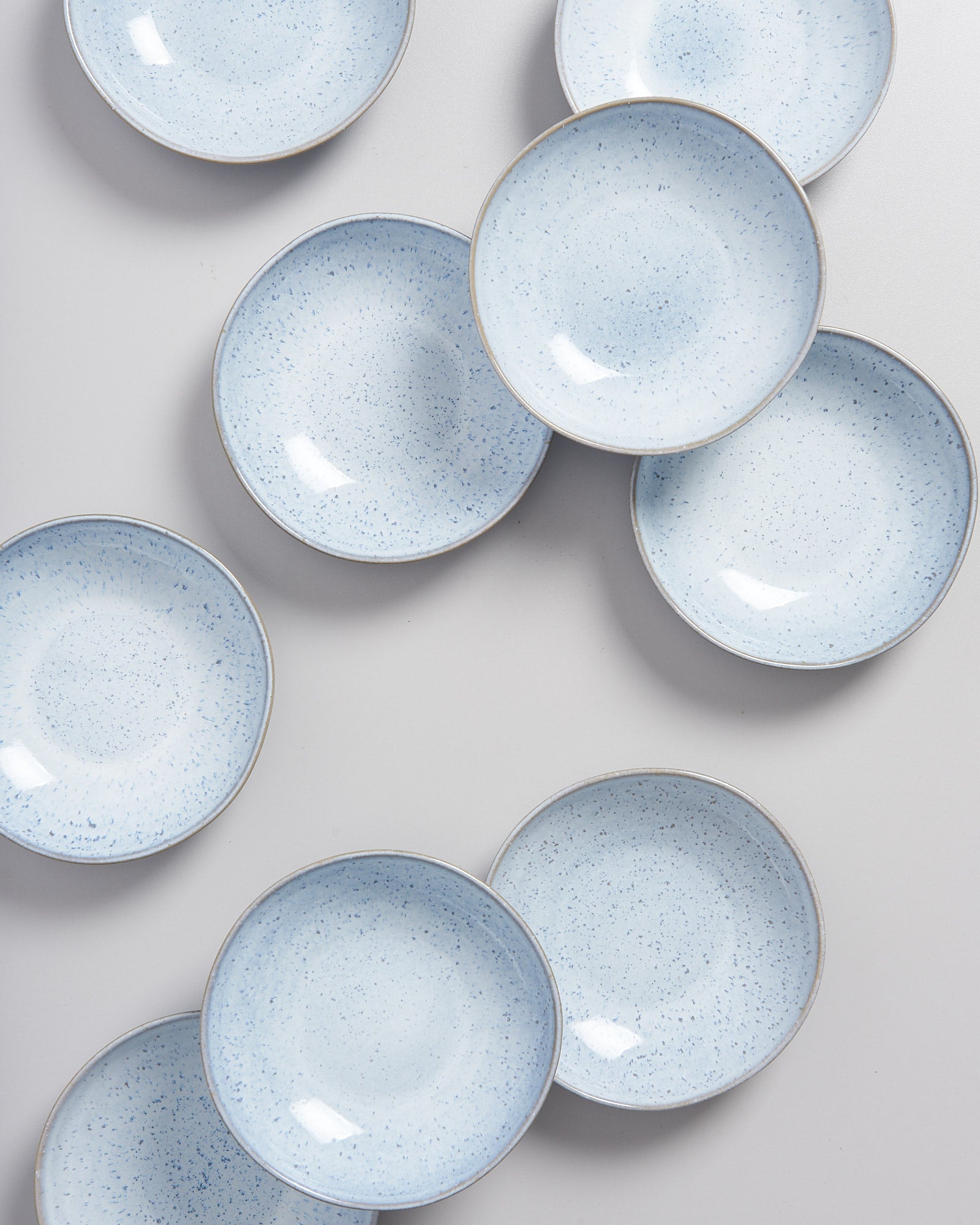 Mehrere blaue Porzellanteller mit feiner Sprenkelung liegen verteilt auf einer weißen Oberfläche.