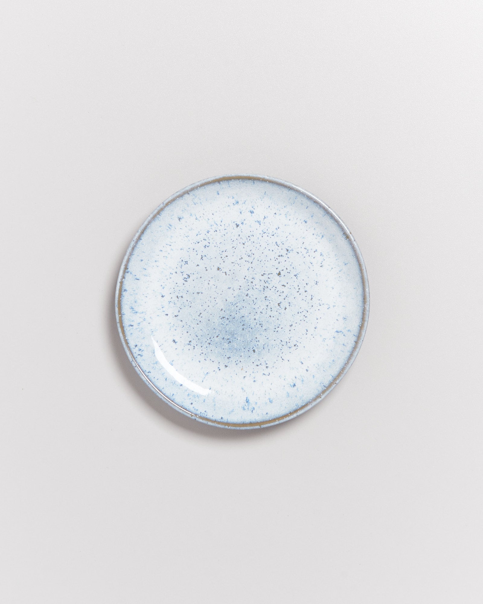 Runder, heller Teller mit blauen Sprenkeln auf weißem Hintergrund.