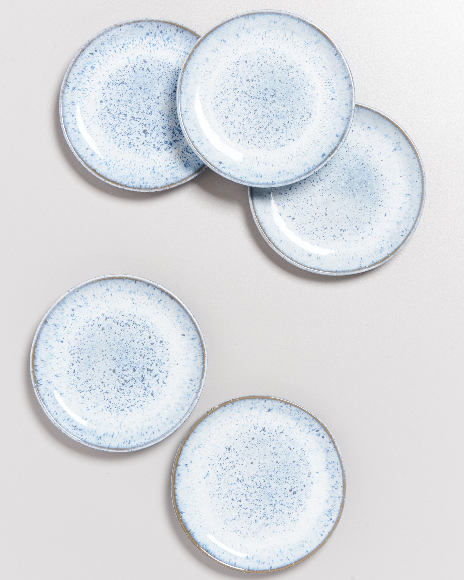 Fünf hellblaue Keramikteller mit gesprenkeltem Muster auf einer weißen Unterlage angeordnet.