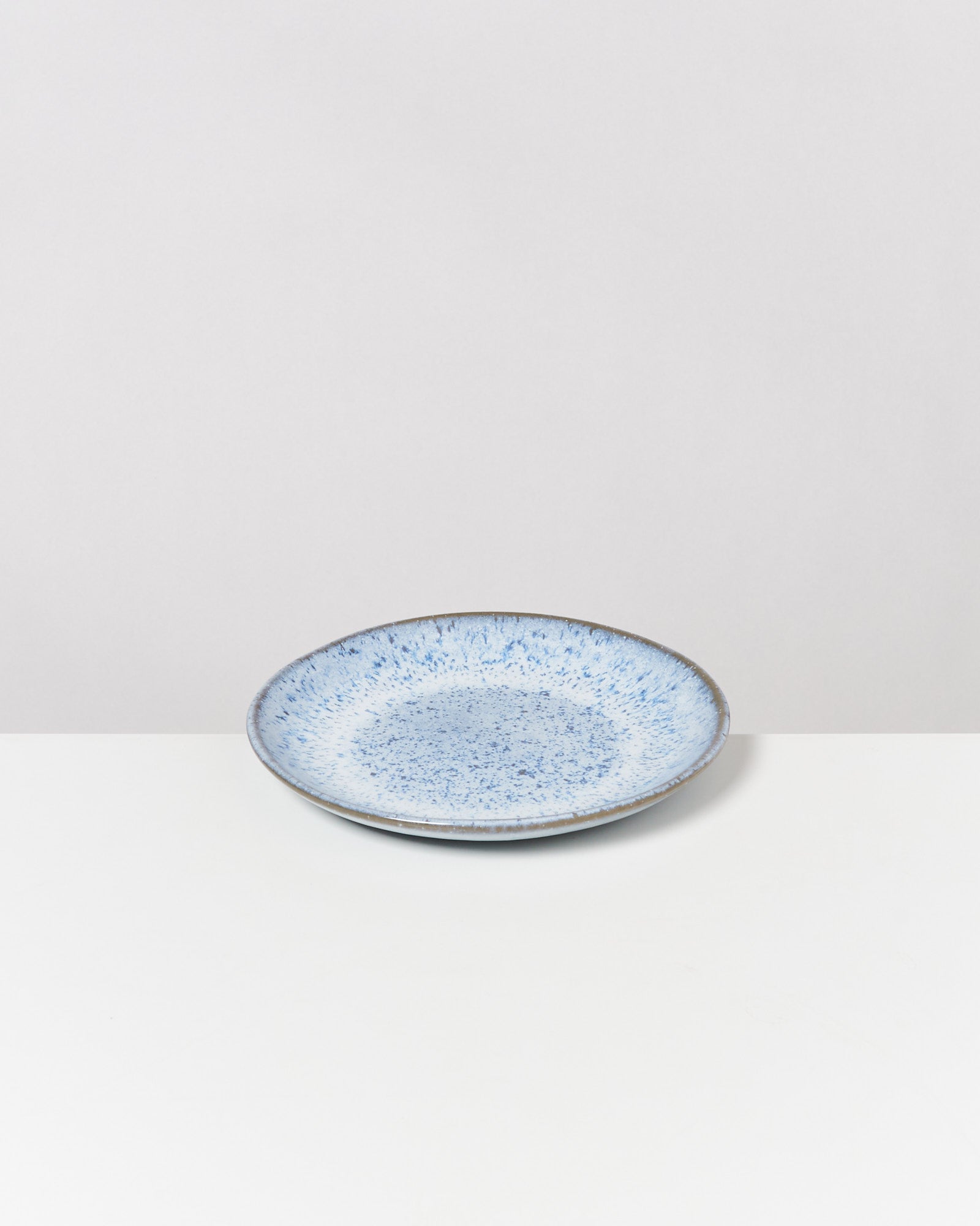 Blauer Keramikteller mit gesprenkeltem Muster auf einem weißen Untergrund vor grauem Hintergrund.