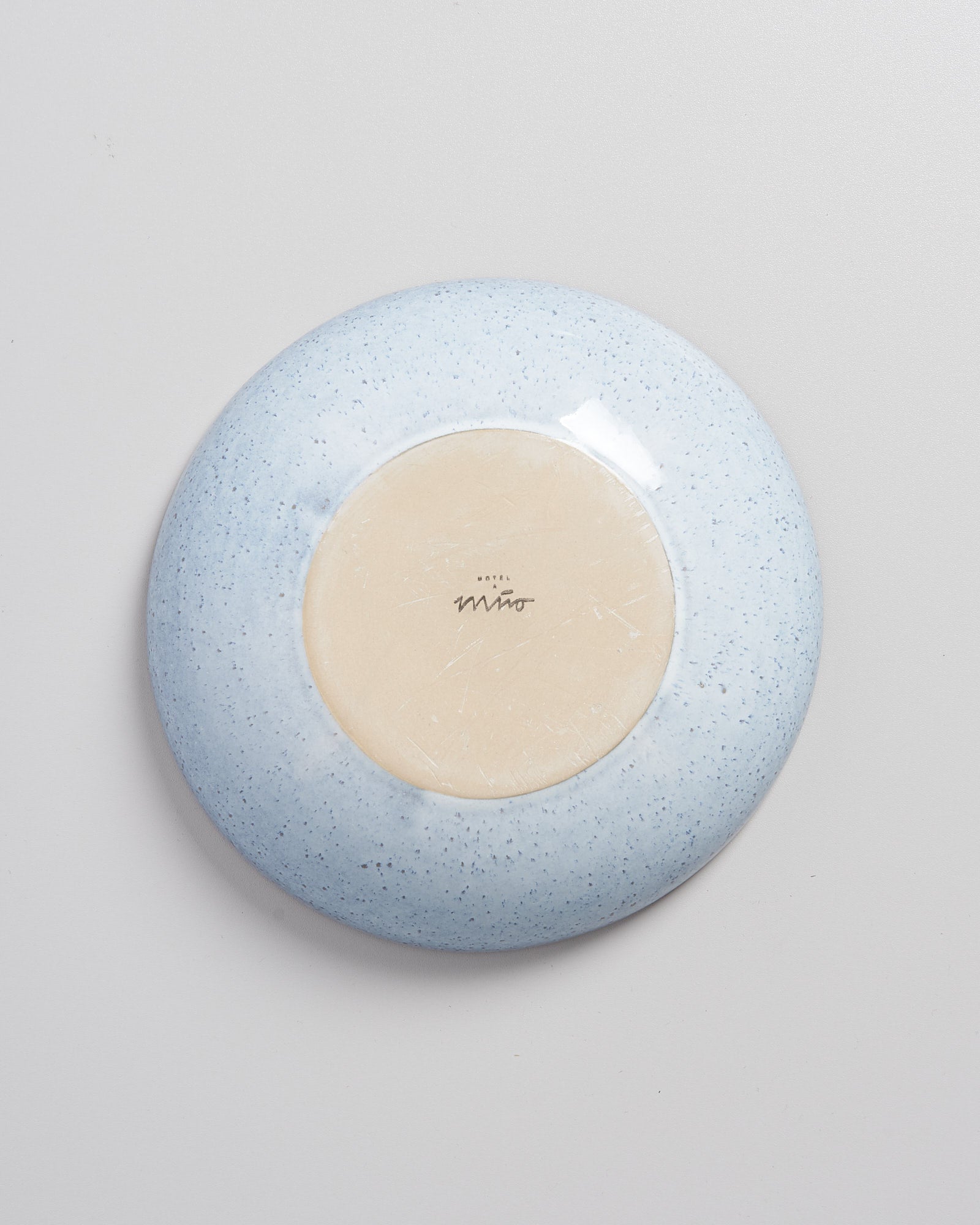 Die Unterseite eines blauen, gesprenkelten Tellers liegt auf einer weißen Oberfläche.