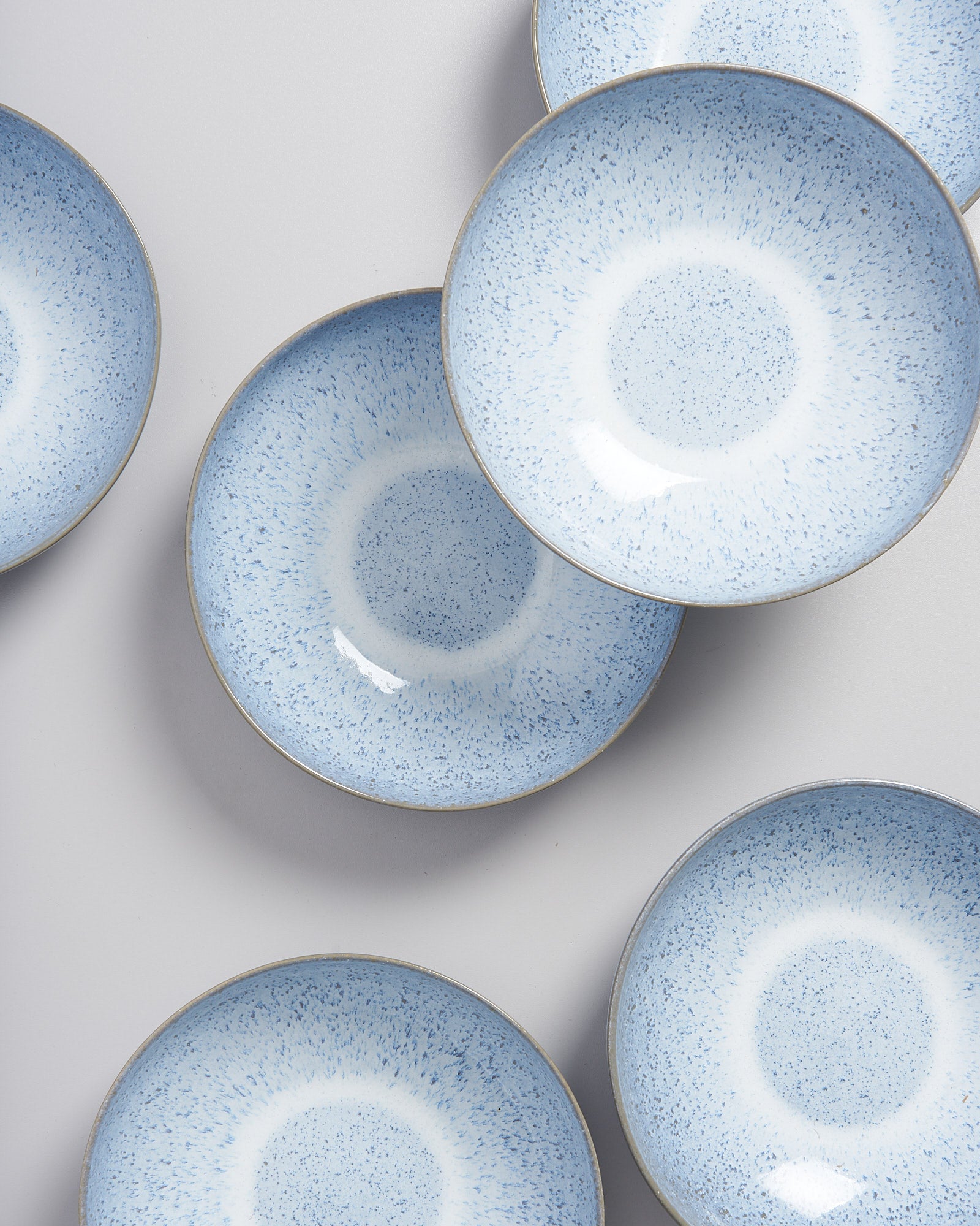 Sechs blau gesprenkelte Keramikteller sind auf einer hellgrauen Oberfläche angeordnet.