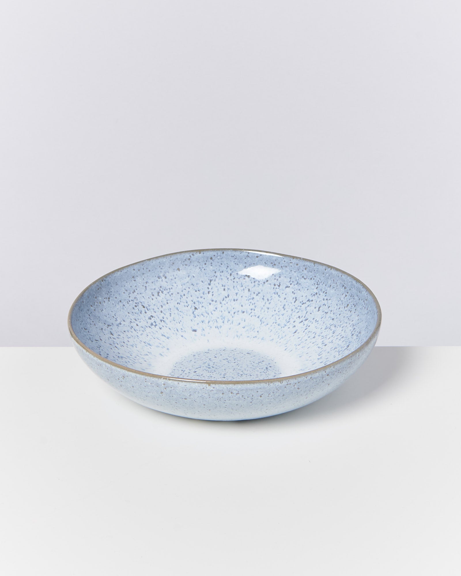 Blaue Keramikschale mit gesprenkelter Oberfläche auf einem weißen Untergrund, vor einem schlichten, grauen Hintergrund.