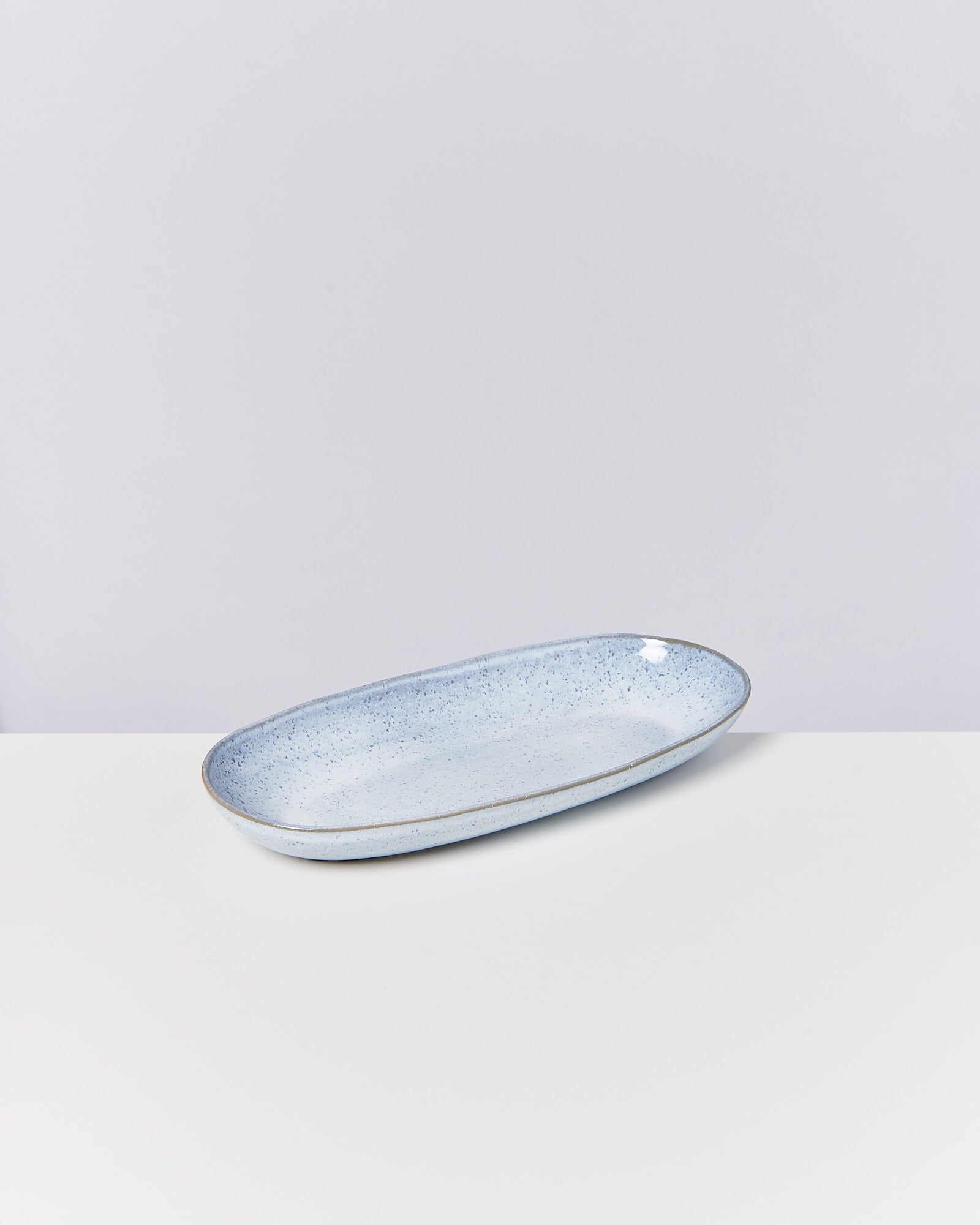 Blau-weiß gesprenkelte, ovale Keramikschale auf einer weißen Oberfläche.