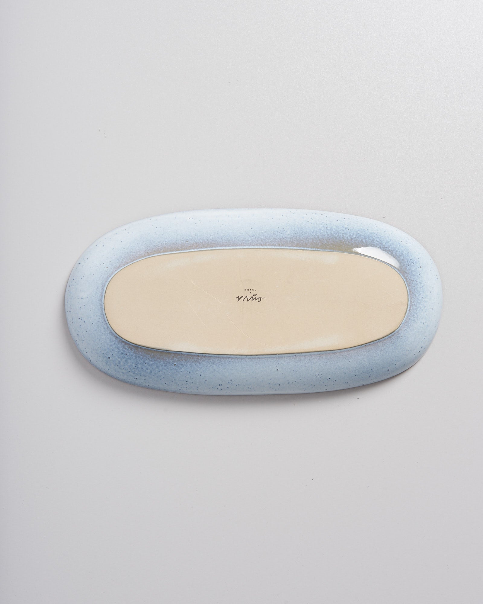Ovale Schale in hellblauem Farbverlauf auf grauem Hintergrund, mit Signatur auf der Unterseite.