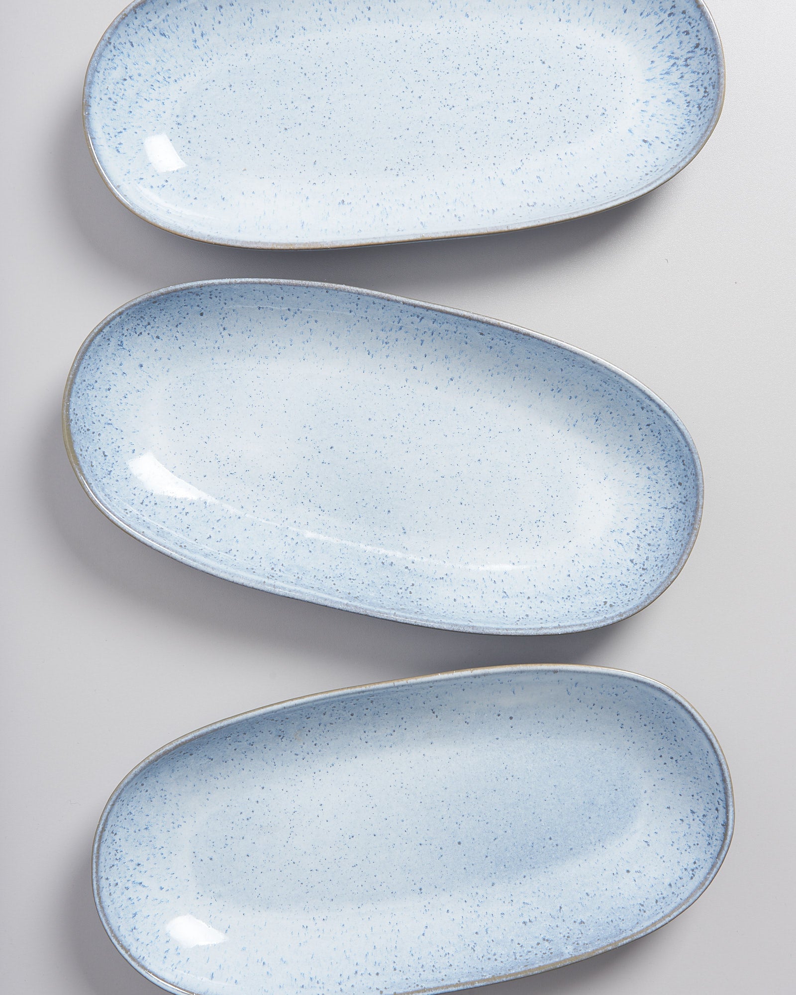 Drei längliche, helle Keramikteller mit blauen Sprenkeln liegen auf einer grauen Oberfläche.