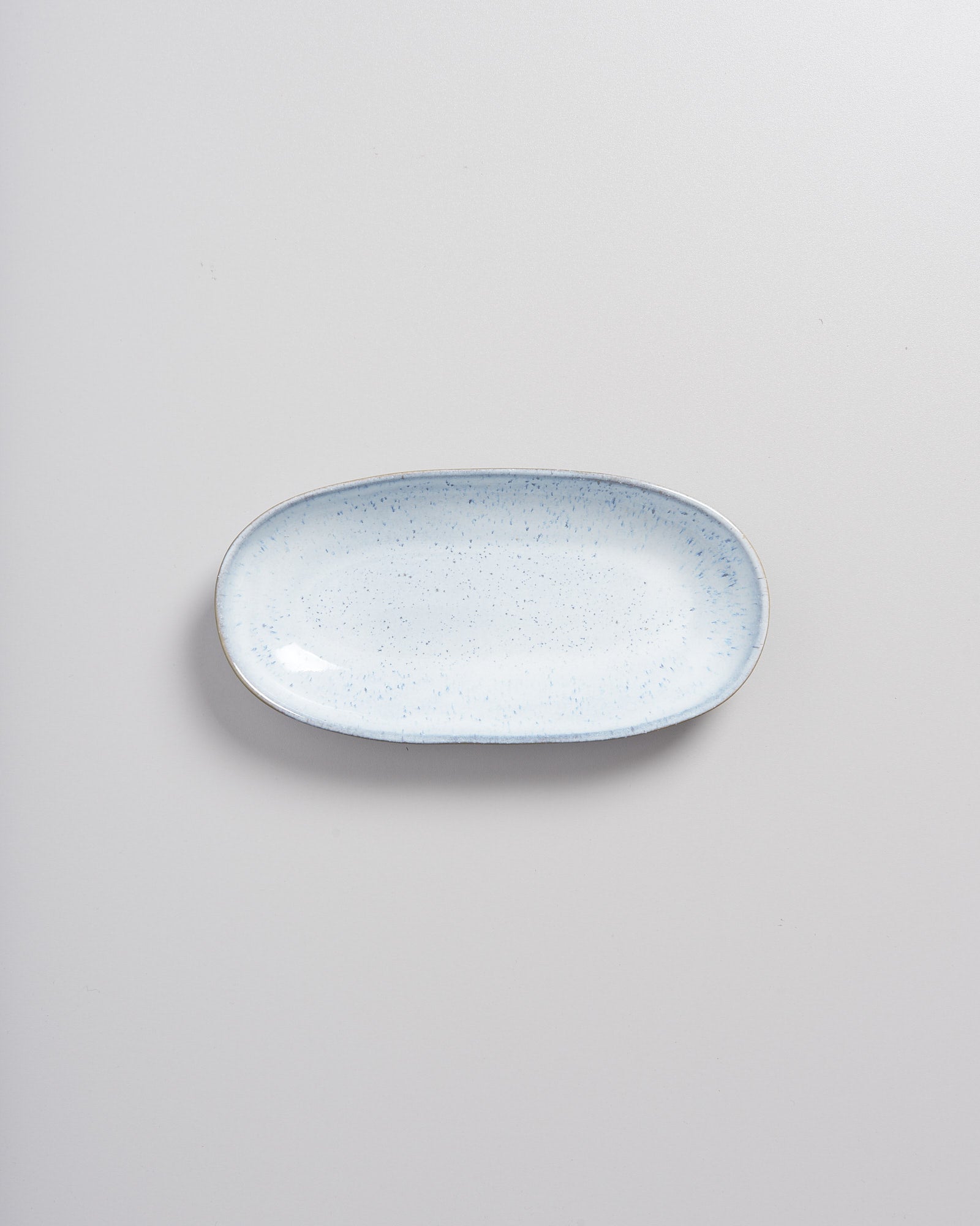 Ovale, hellblaue Keramikschale mit dunklen Sprenkeln auf hellem Hintergrund.