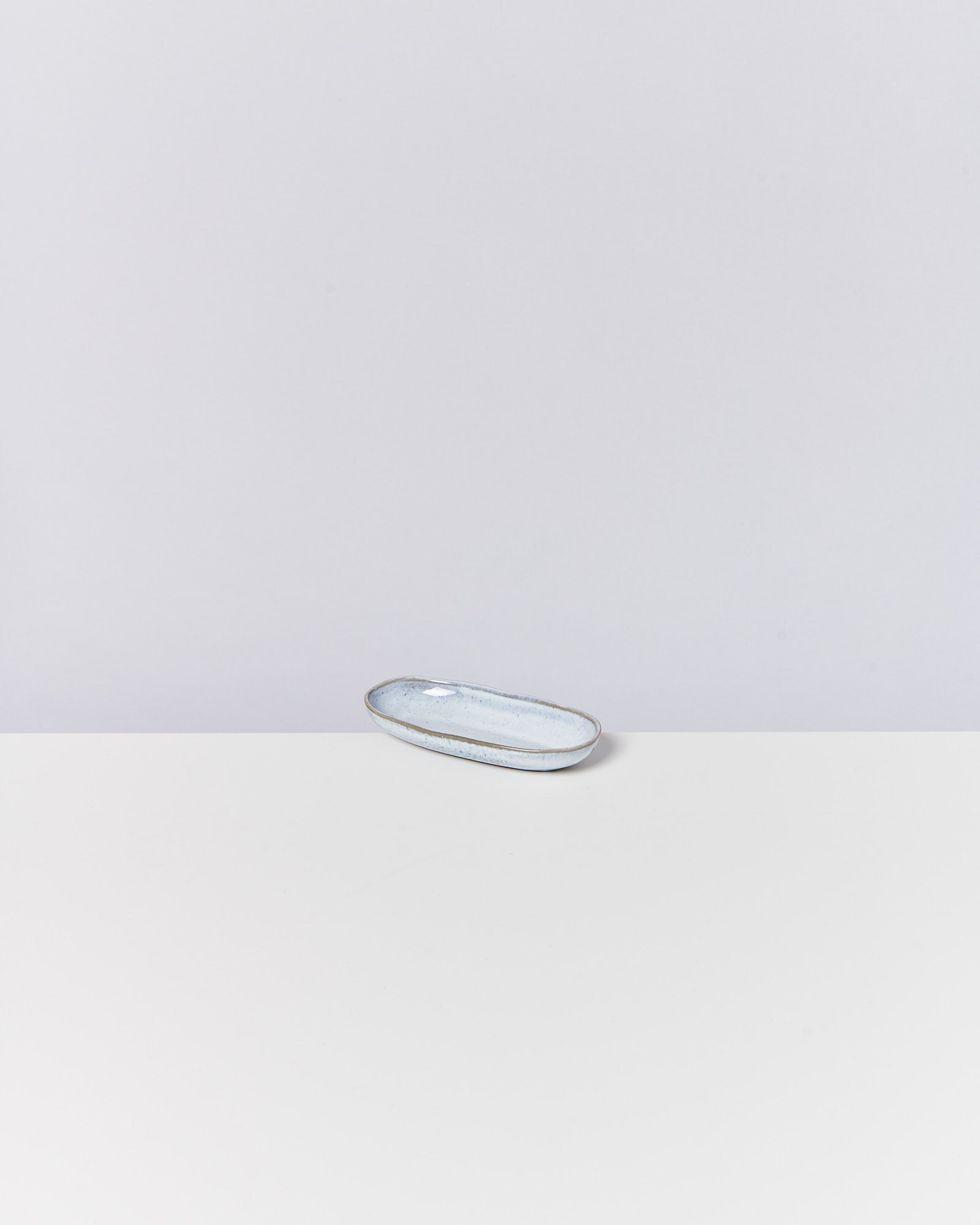 Ein kleines, ovales, hellblaues Keramikschälchen auf einem weißen Tisch vor grauem Hintergrund.