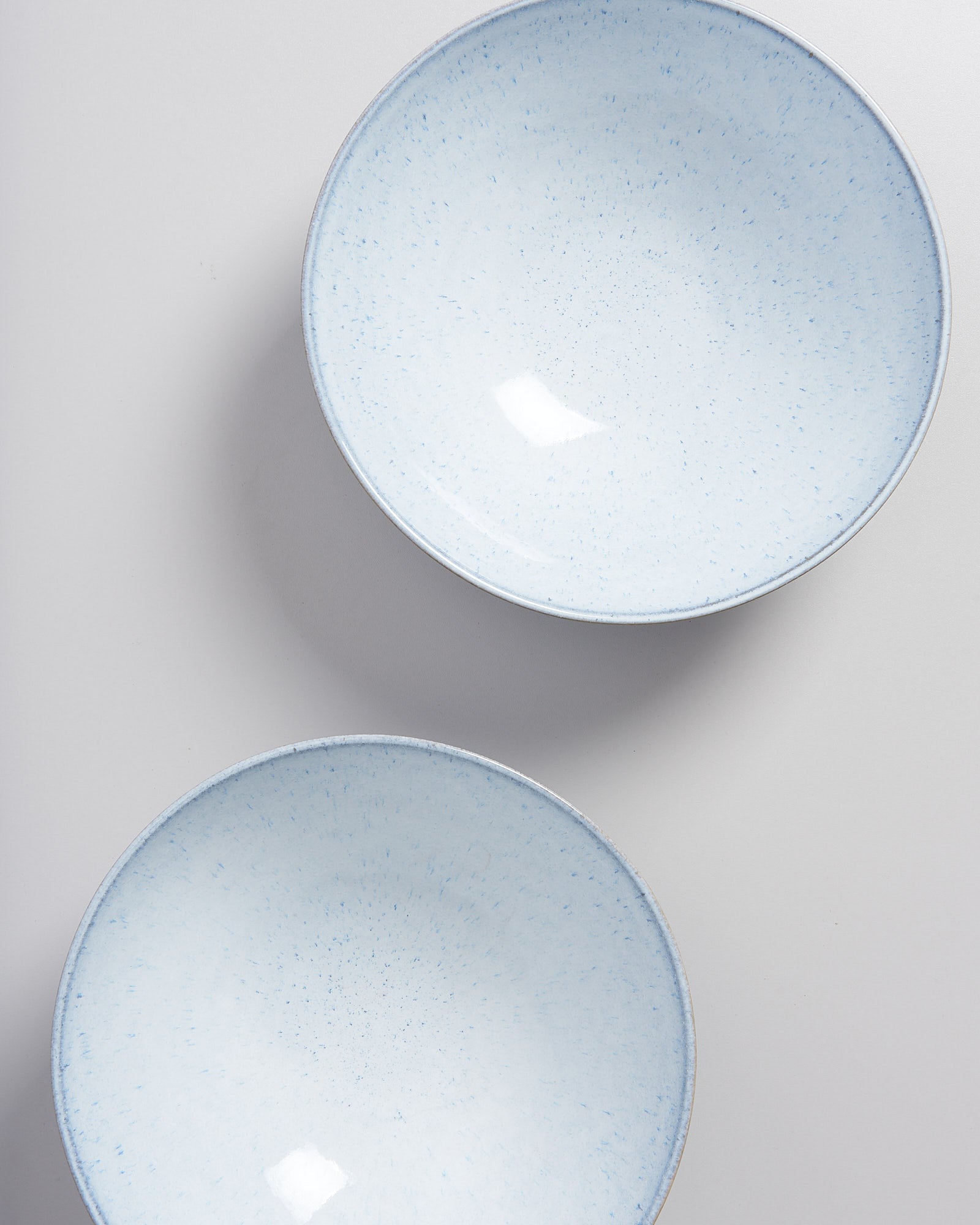 Zwei hellblaue Keramikschalen mit feinen Sprenkeln auf grauem Hintergrund.