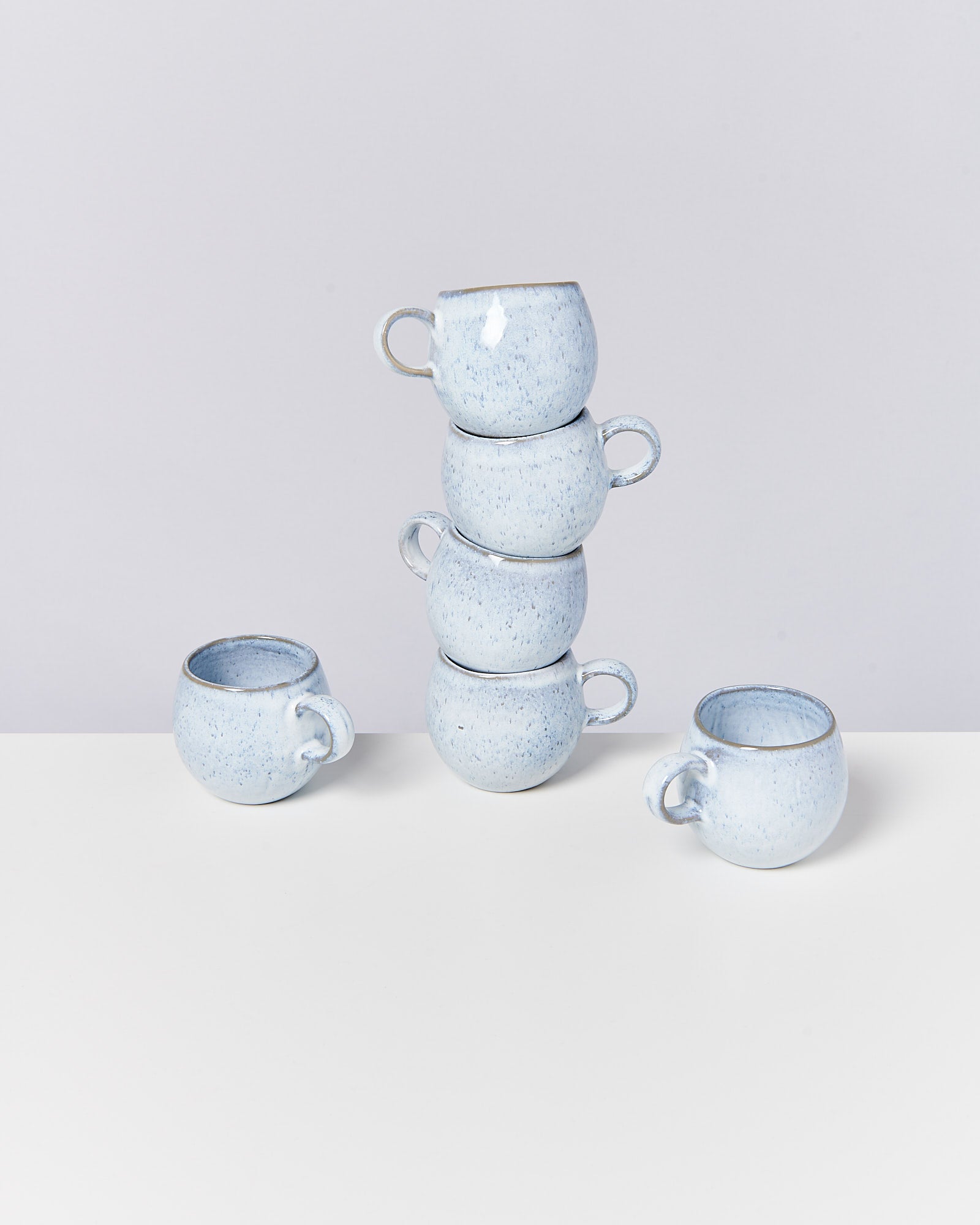 Fünf hellblaue Tassen, drei davon gestapelt, stehen auf einem weißen Untergrund.