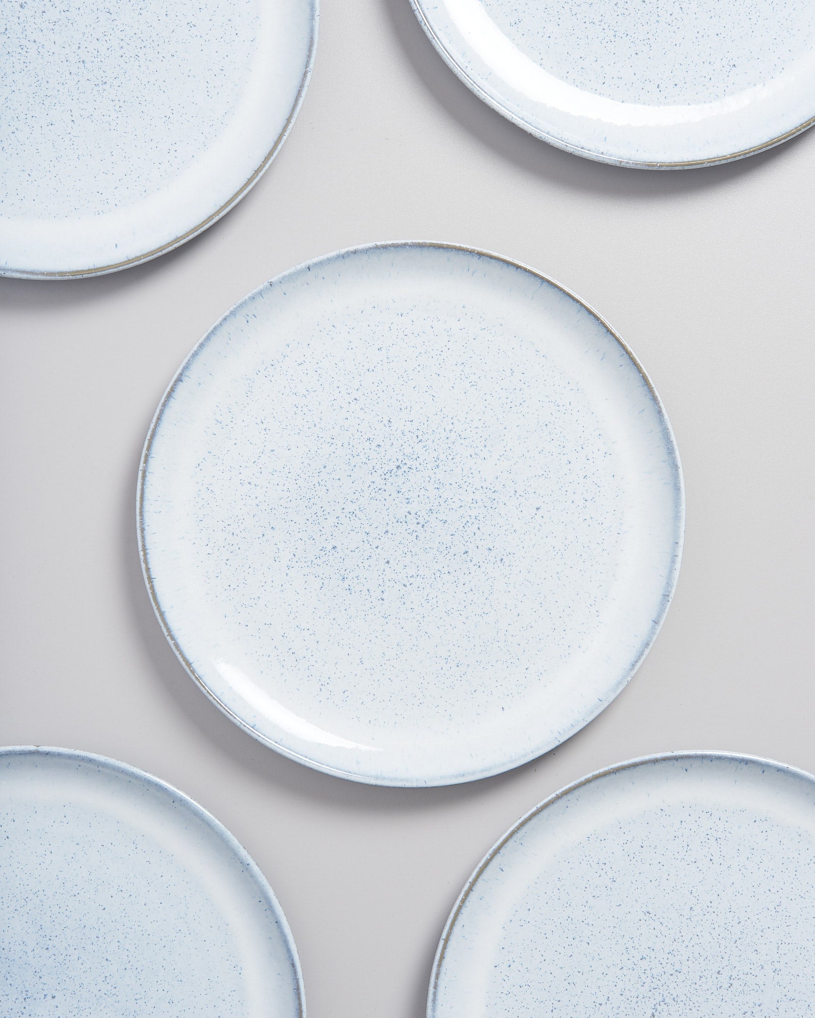 Fünf weiße Teller mit blauen Sprenkeln liegen auf einer grauen Oberfläche.