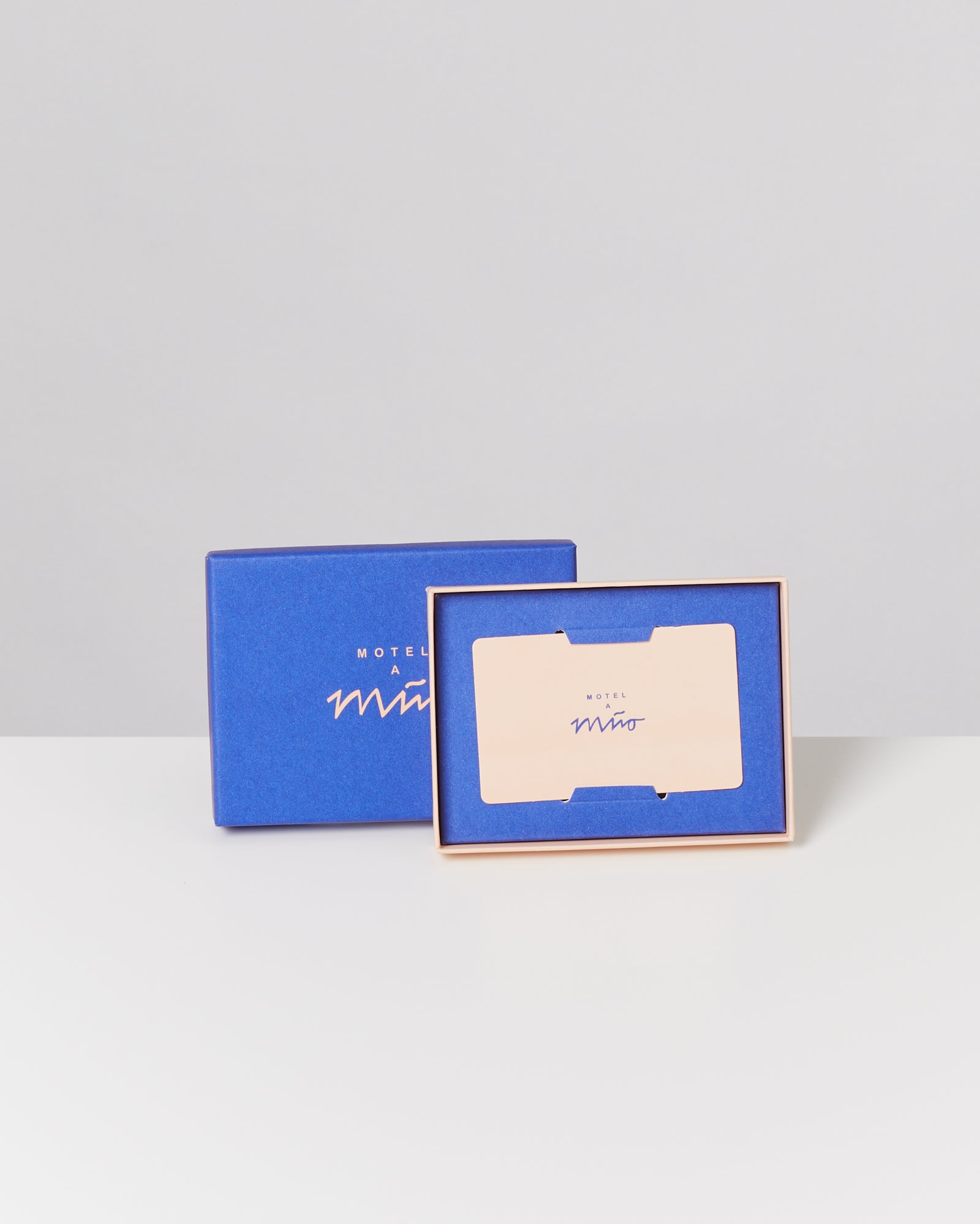 Blaue Geschenkbox und Geschenkkarte mit Aufschrift "Motel a Miio" auf hellem Hintergrund.