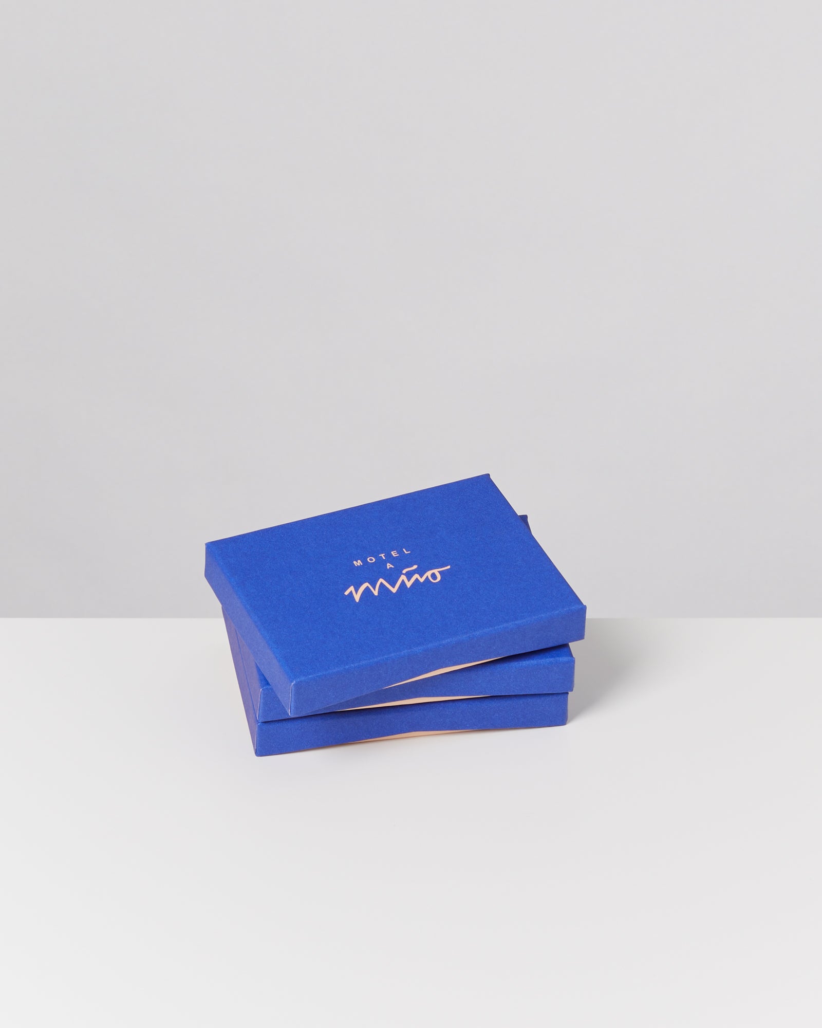 Zwei gestapelte blaue Schachteln mit dem Schriftzug "Motel a Miio" auf einem weißen Hintergrund.