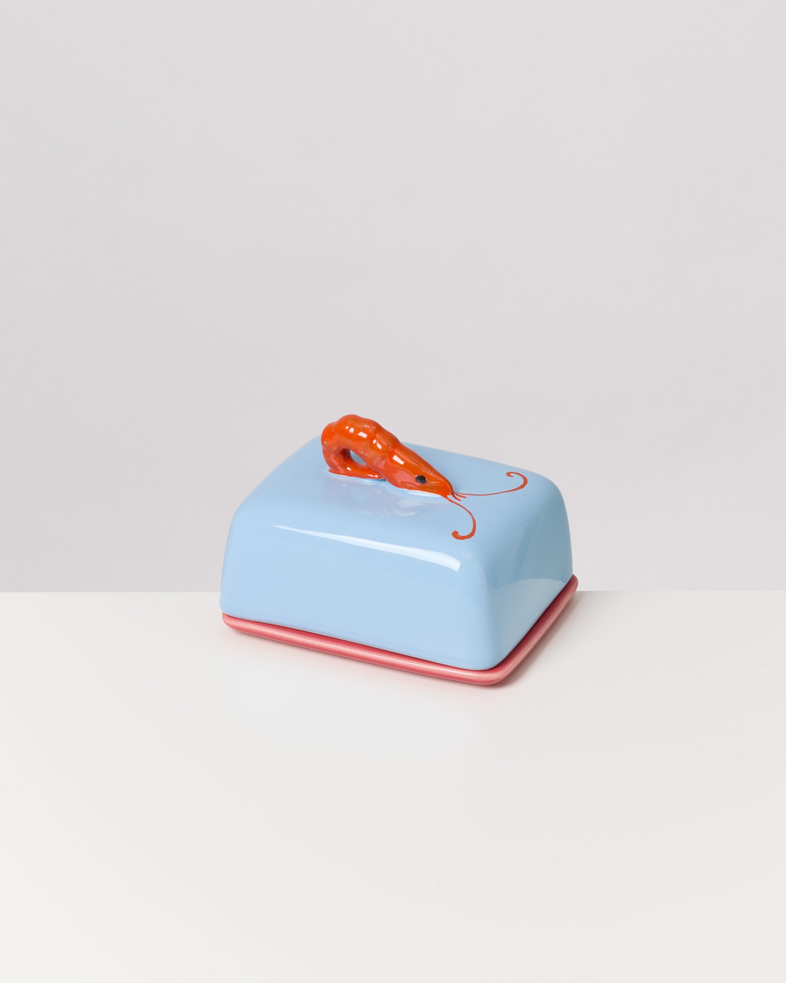 Blaue Butterdose mit orangefarbenem Krabben-Designgriff auf einem weißen Tisch.
