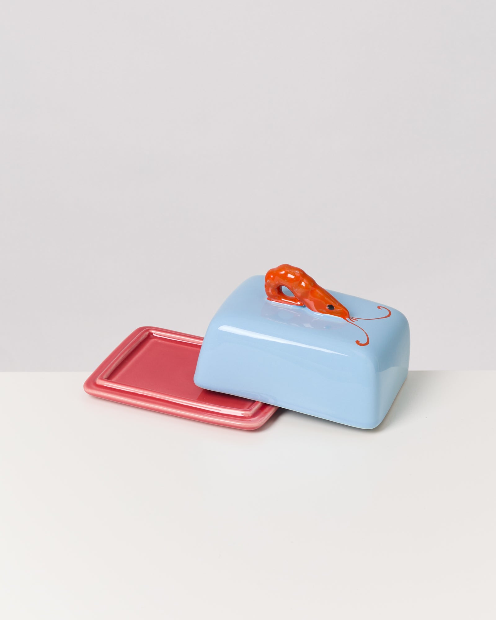 Blaue Butterdose mit rotem Käfergriff auf einem rosa Tablett.