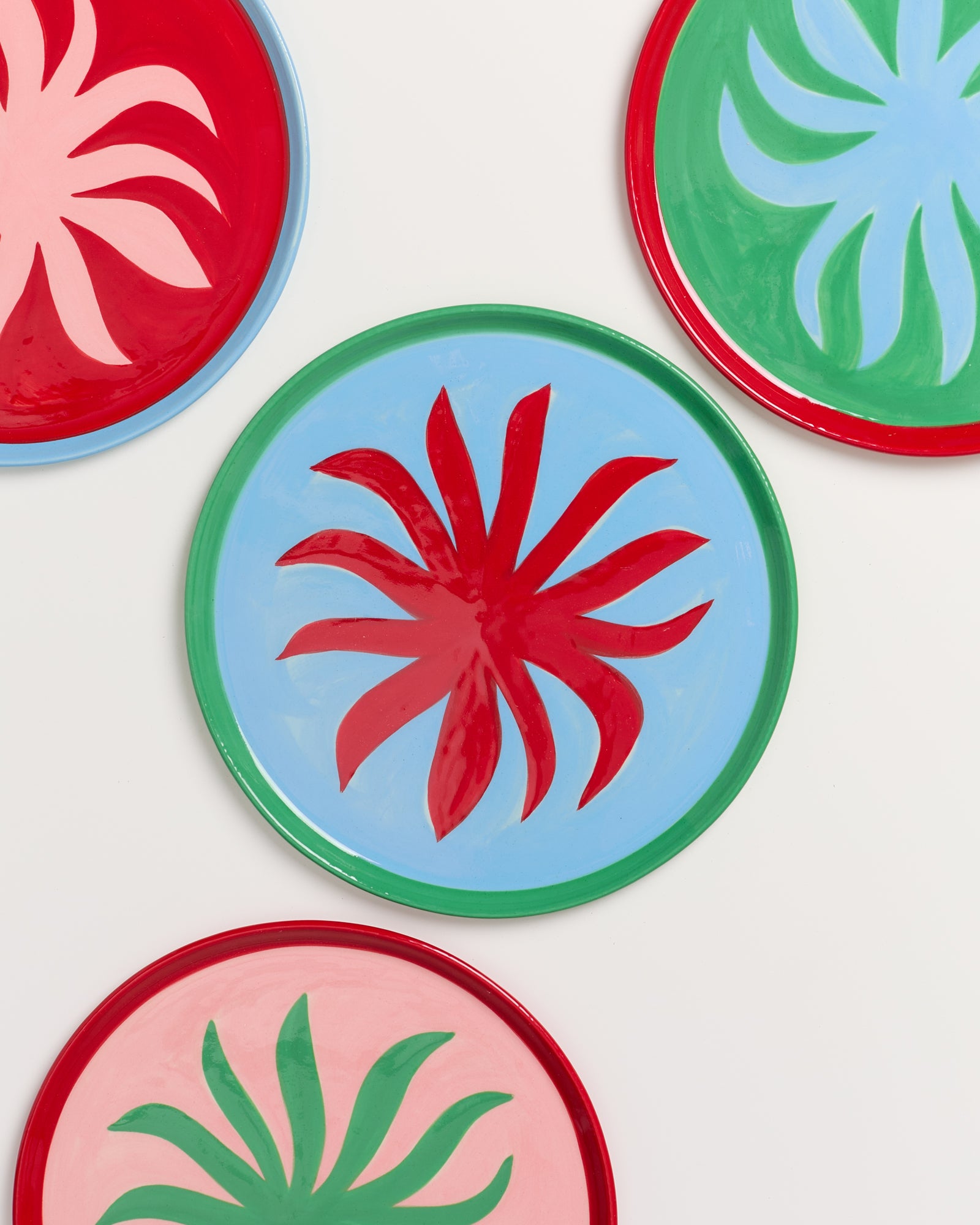Vier bunte Teller mit abstrakten Palmenmustern in Rot, Grün, Blau und Rosa auf weißem Hintergrund.