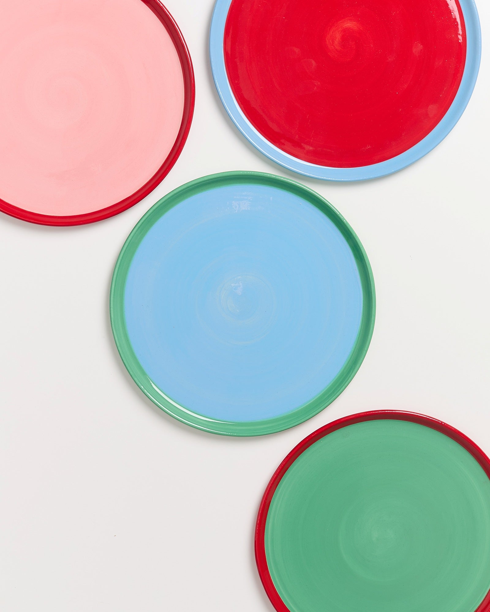 Vier bunte, runde Teller mit roten, blauen, grünen und rosa Farbakzenten auf weißem Hintergrund.