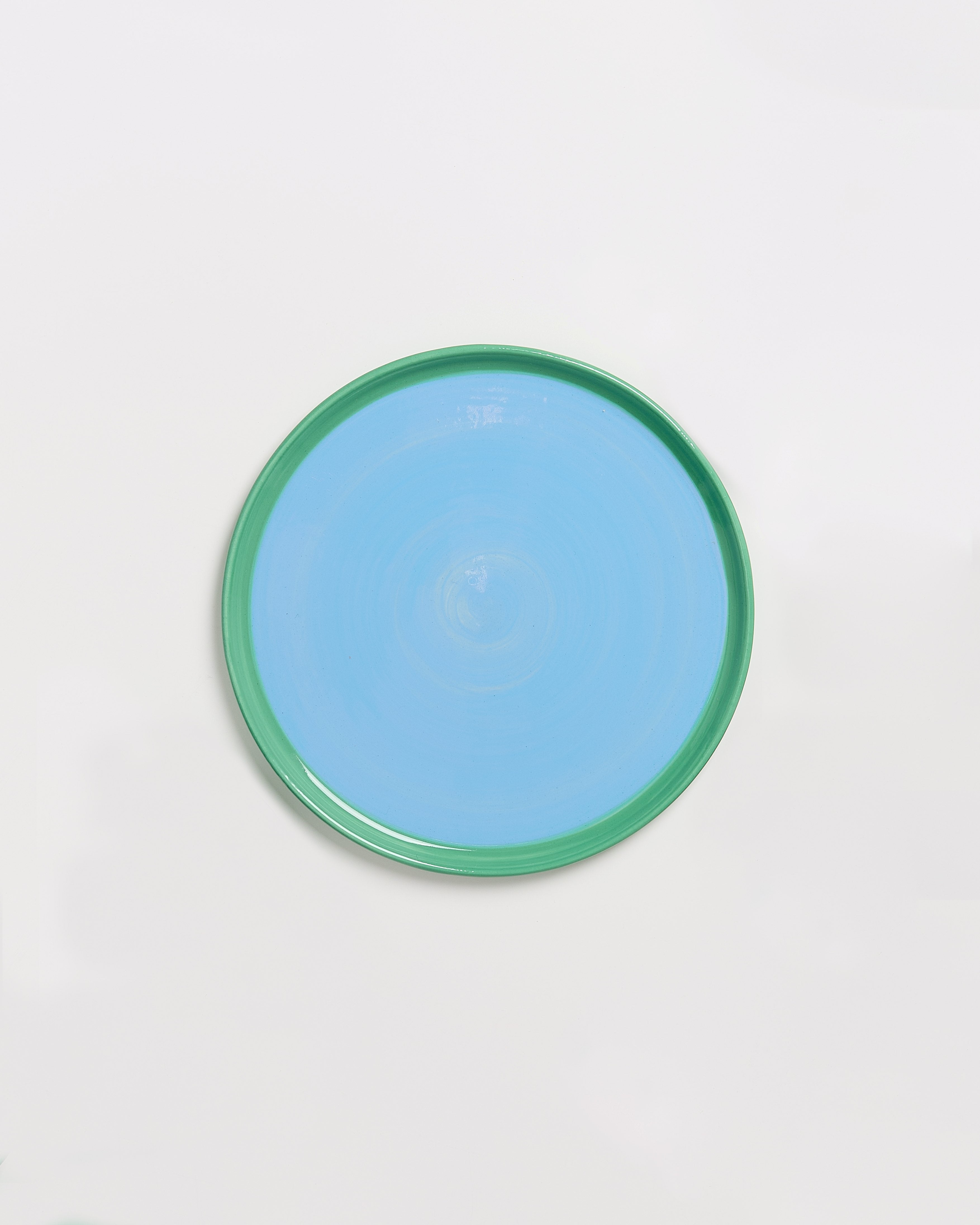 Runde, flache, blau-grüne Keramikschale auf weißem Hintergrund.