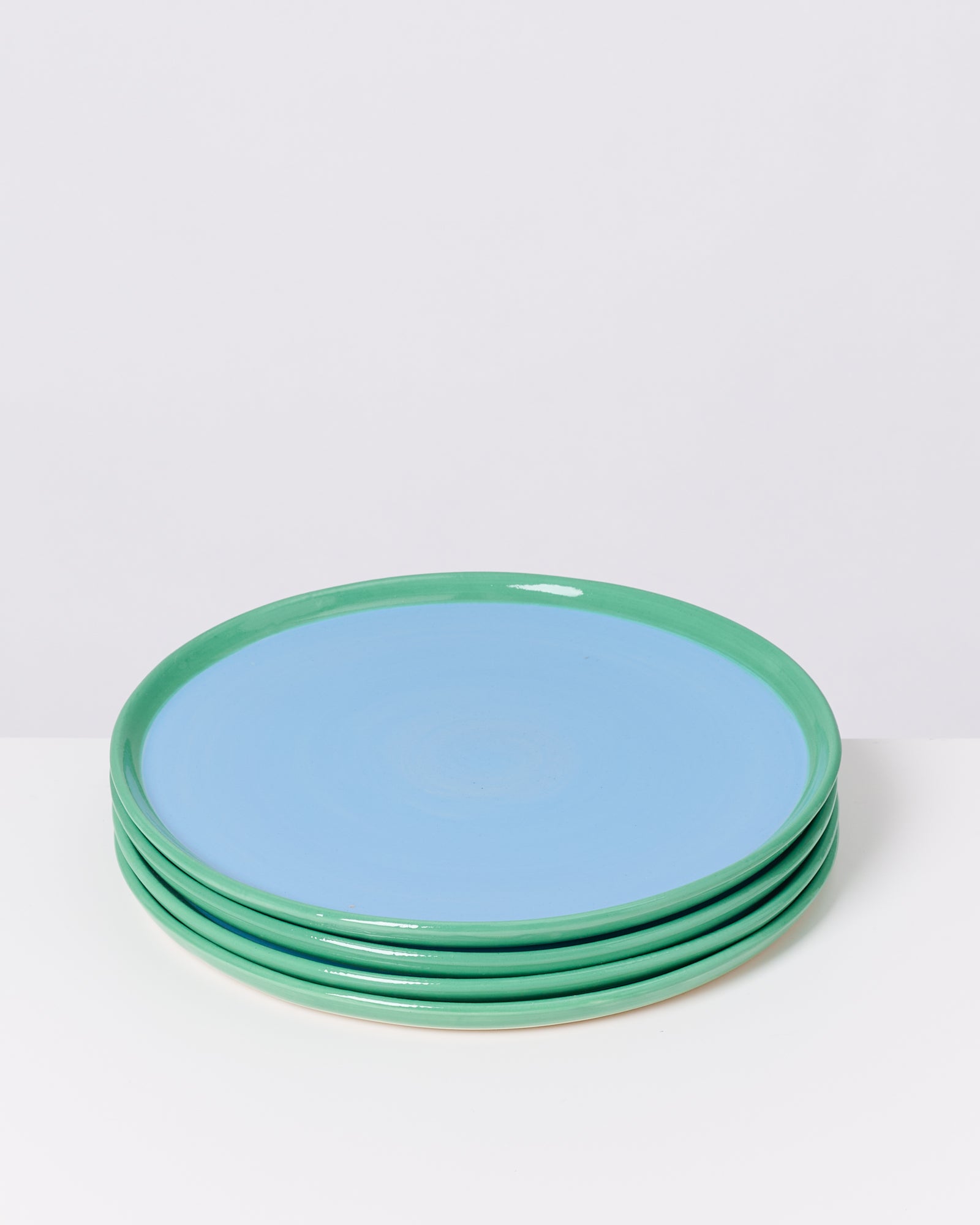 Ein Stapel von fünf Tellern mit blauer Mitte und grünem Rand auf einem weißen Hintergrund.