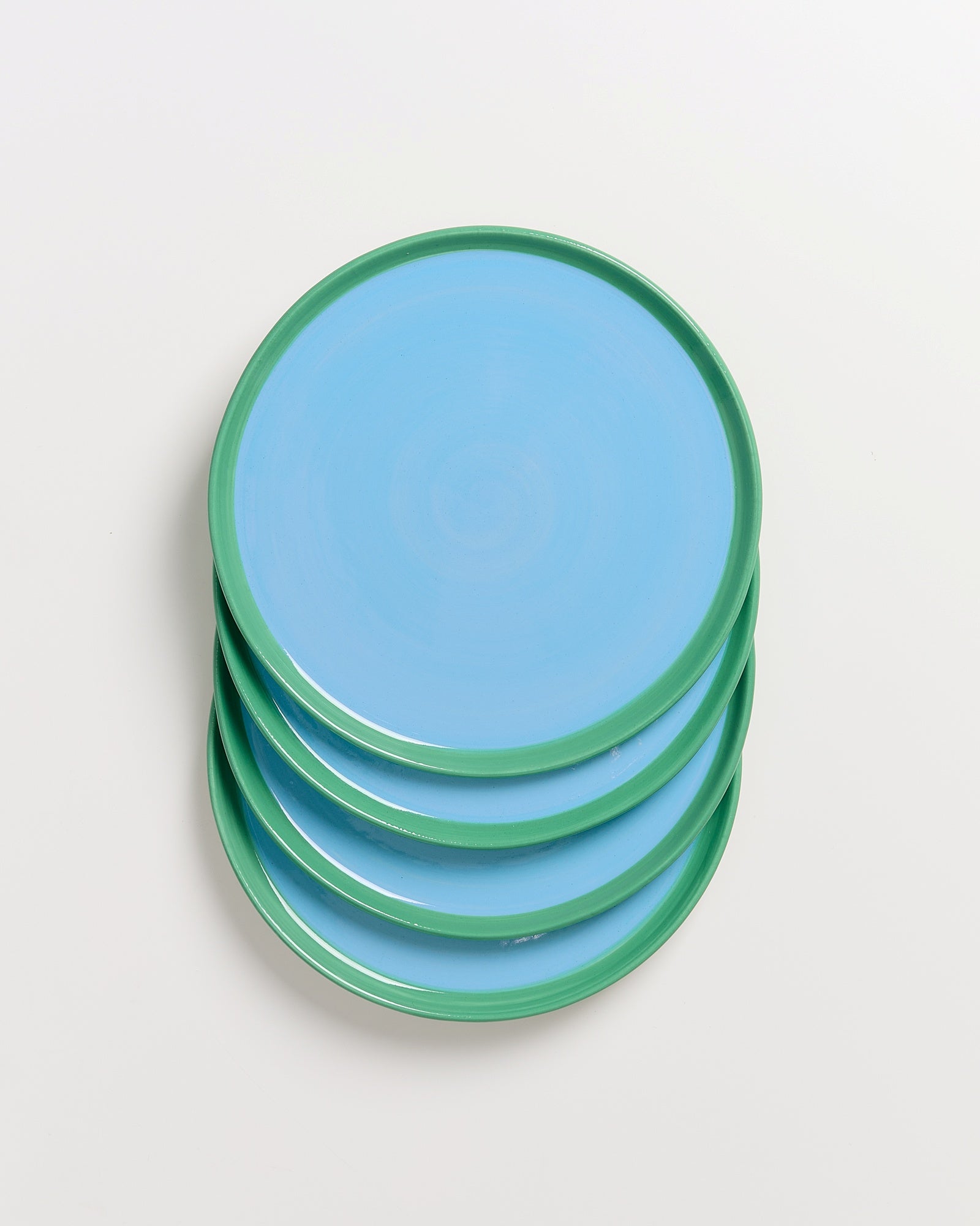 Ein Stapel aus vier hellblauen Tellern mit grünem Rand auf einem weißen Hintergrund.