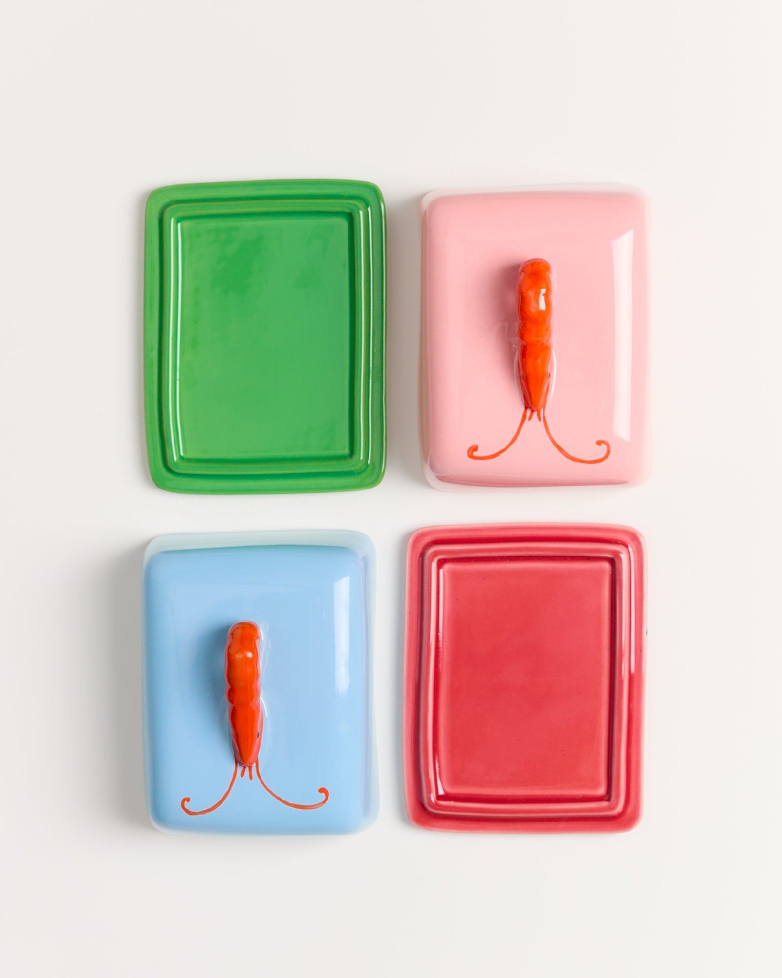 Vier bunte rechteckige Schalen; grün, hellblau, rosa und rot; zwei mit Orangenskulpturen auf rosa und blau.