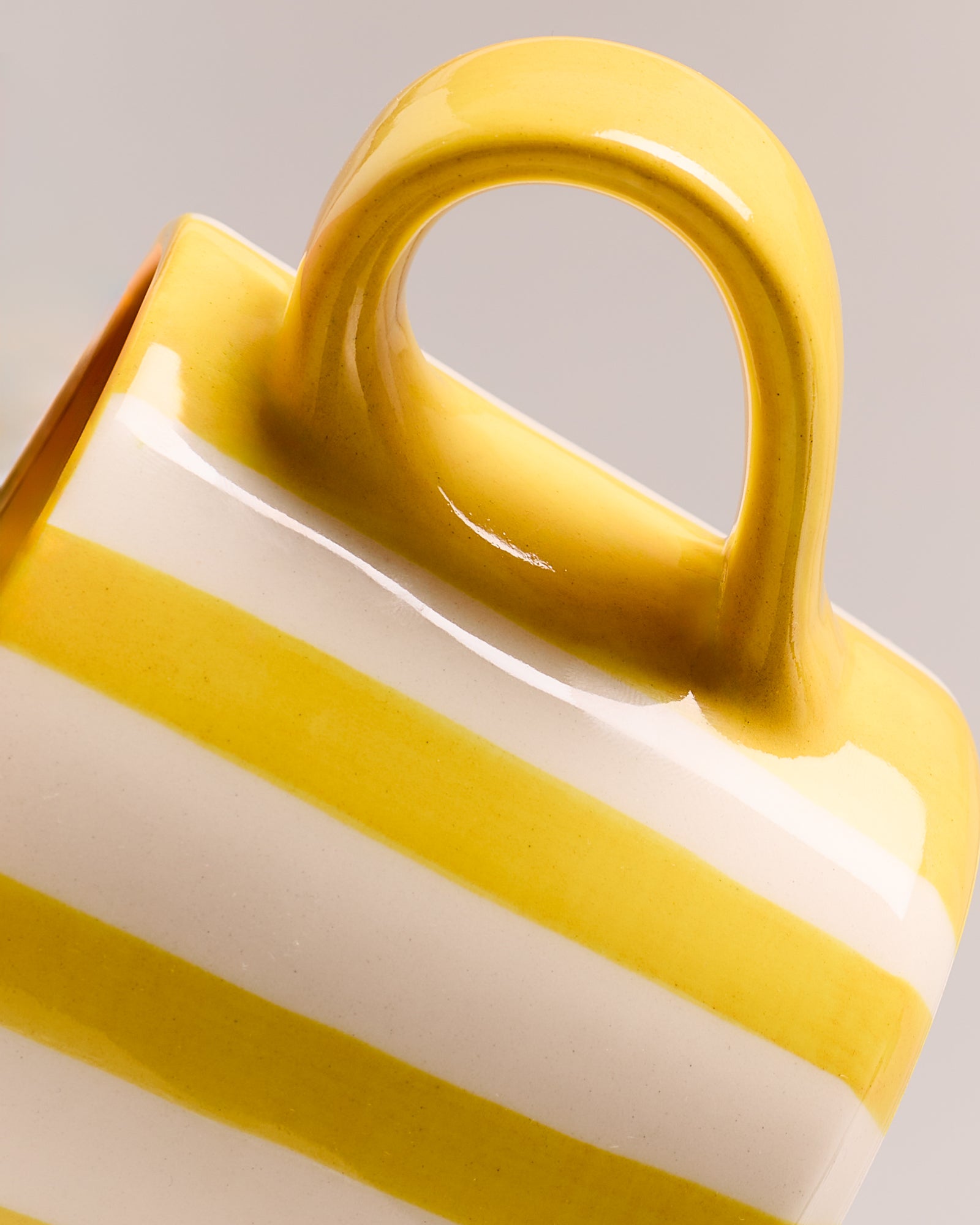 Nahaufnahme einer Tasse mit gelben und weißen Streifen vor einem grauen Hintergrund.