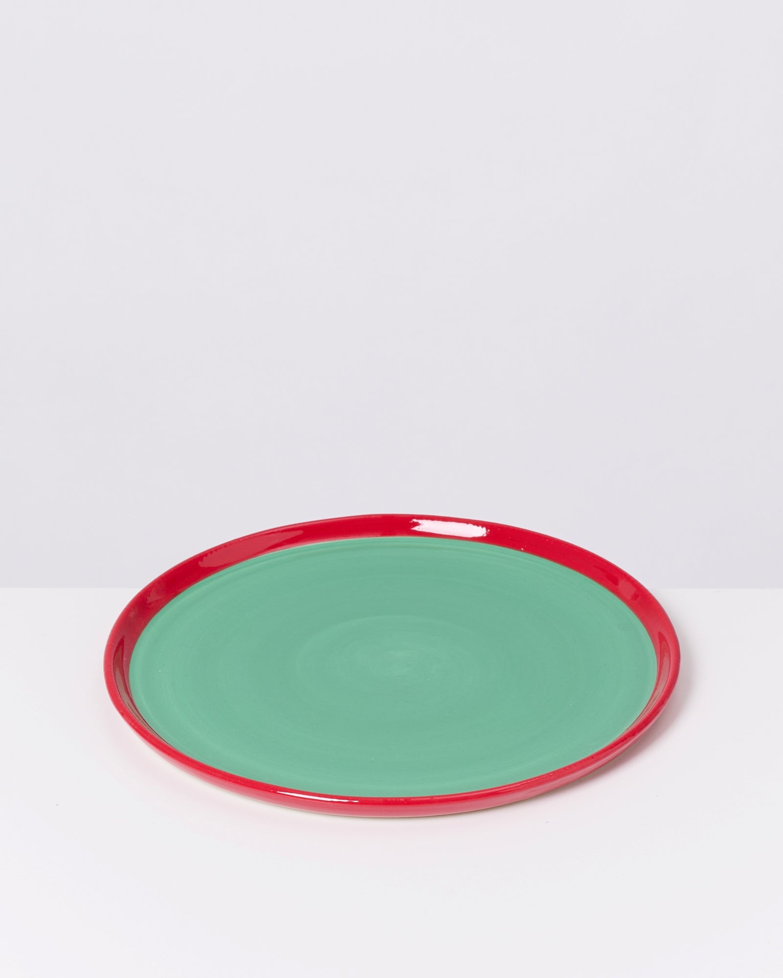 Ein runder Teller mit grüner Oberfläche und rotem Rand auf einem weißen Hintergrund.