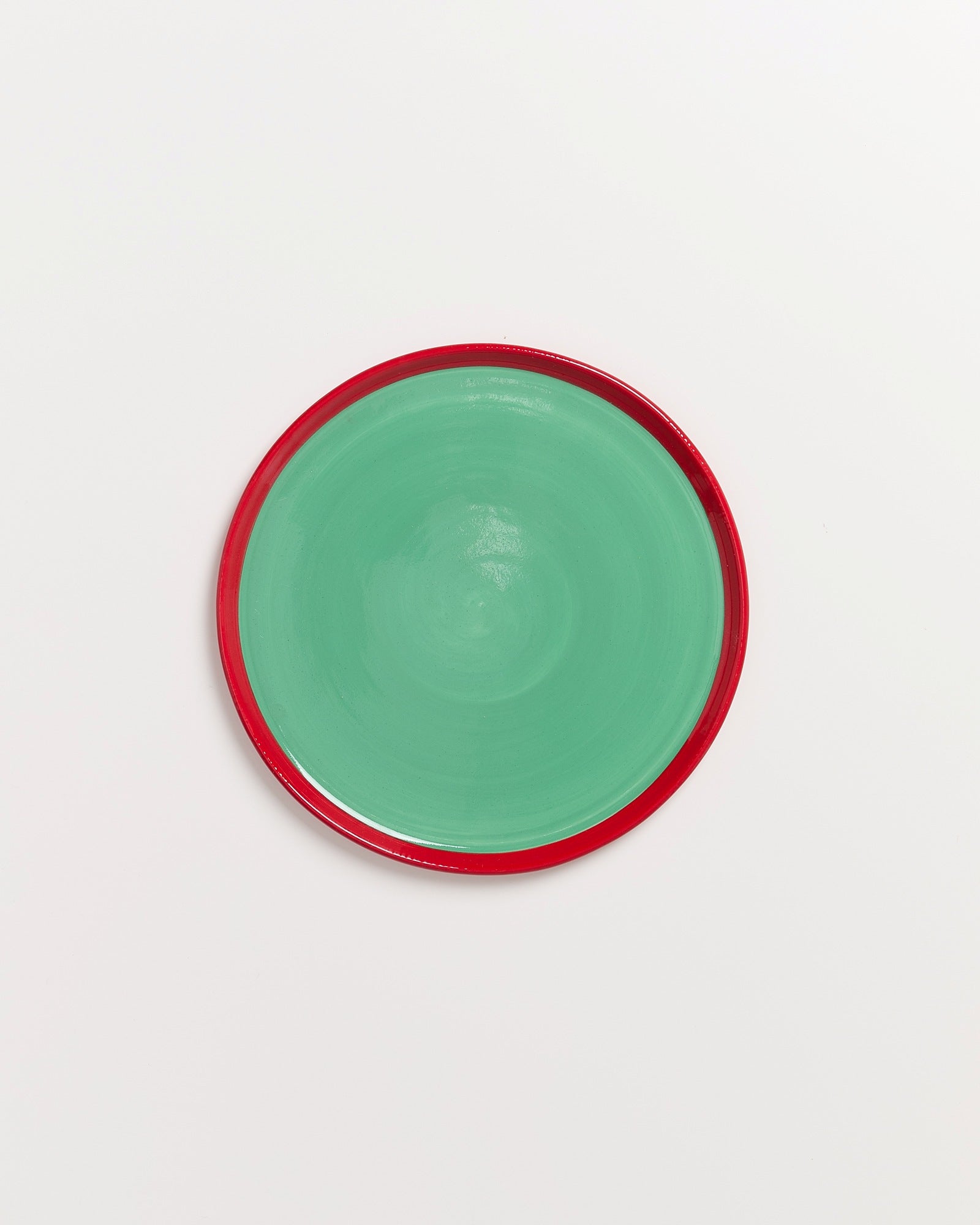 Runder Teller mit grünem Zentrum und rotem Rand auf weißem Hintergrund.