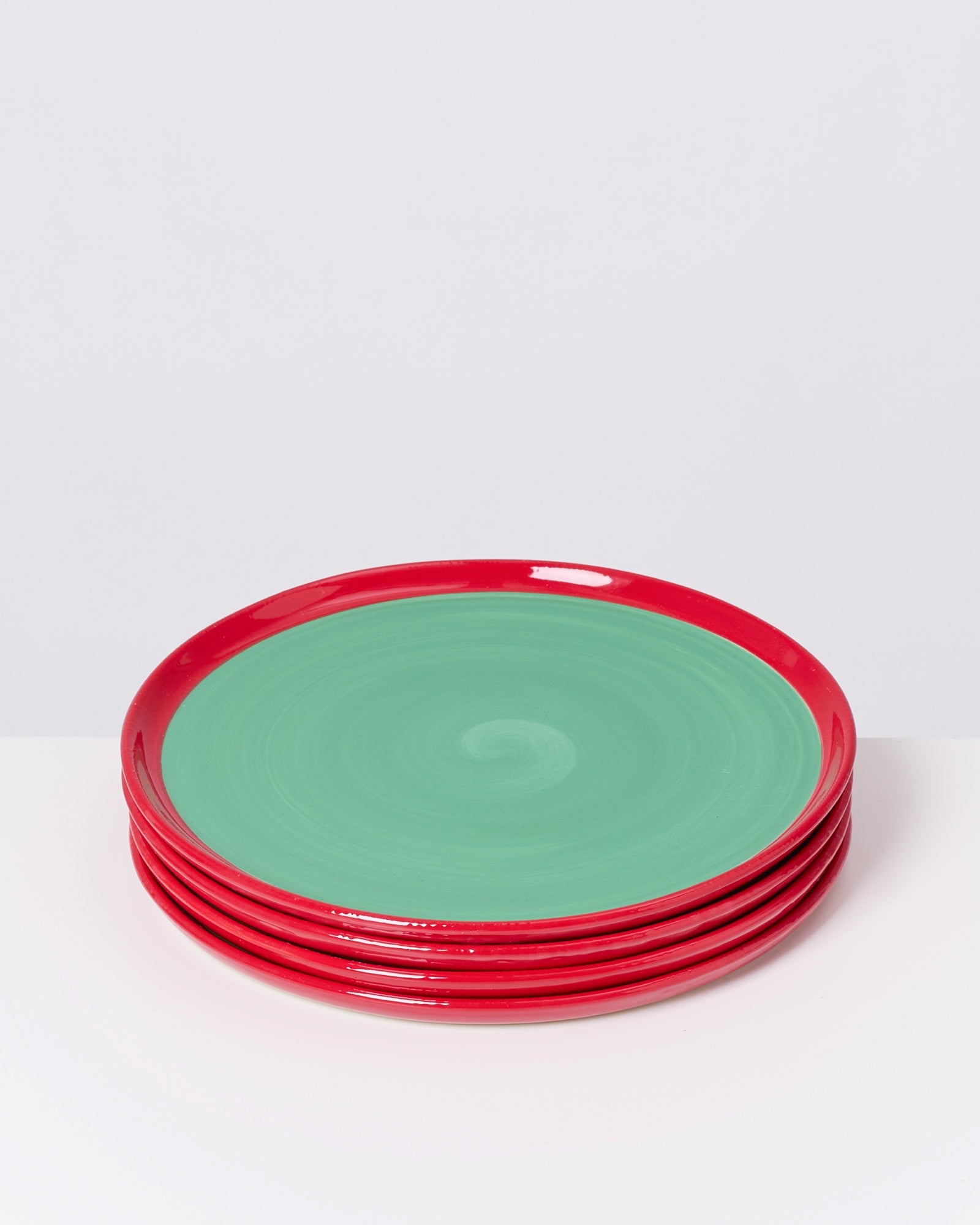 Fünf gestapelte Teller mit roten Rändern und grünen Innenseiten auf hellem Hintergrund.