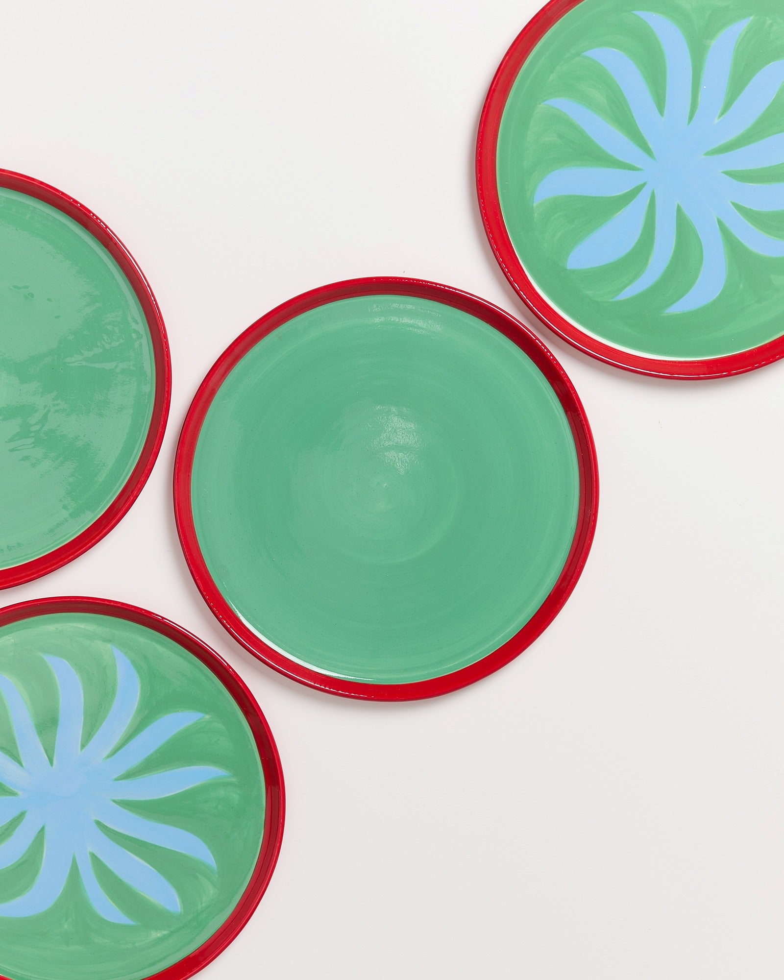Vier grüne Teller mit roten Rändern auf weißem Hintergrund, zwei mit blauen Mustern.