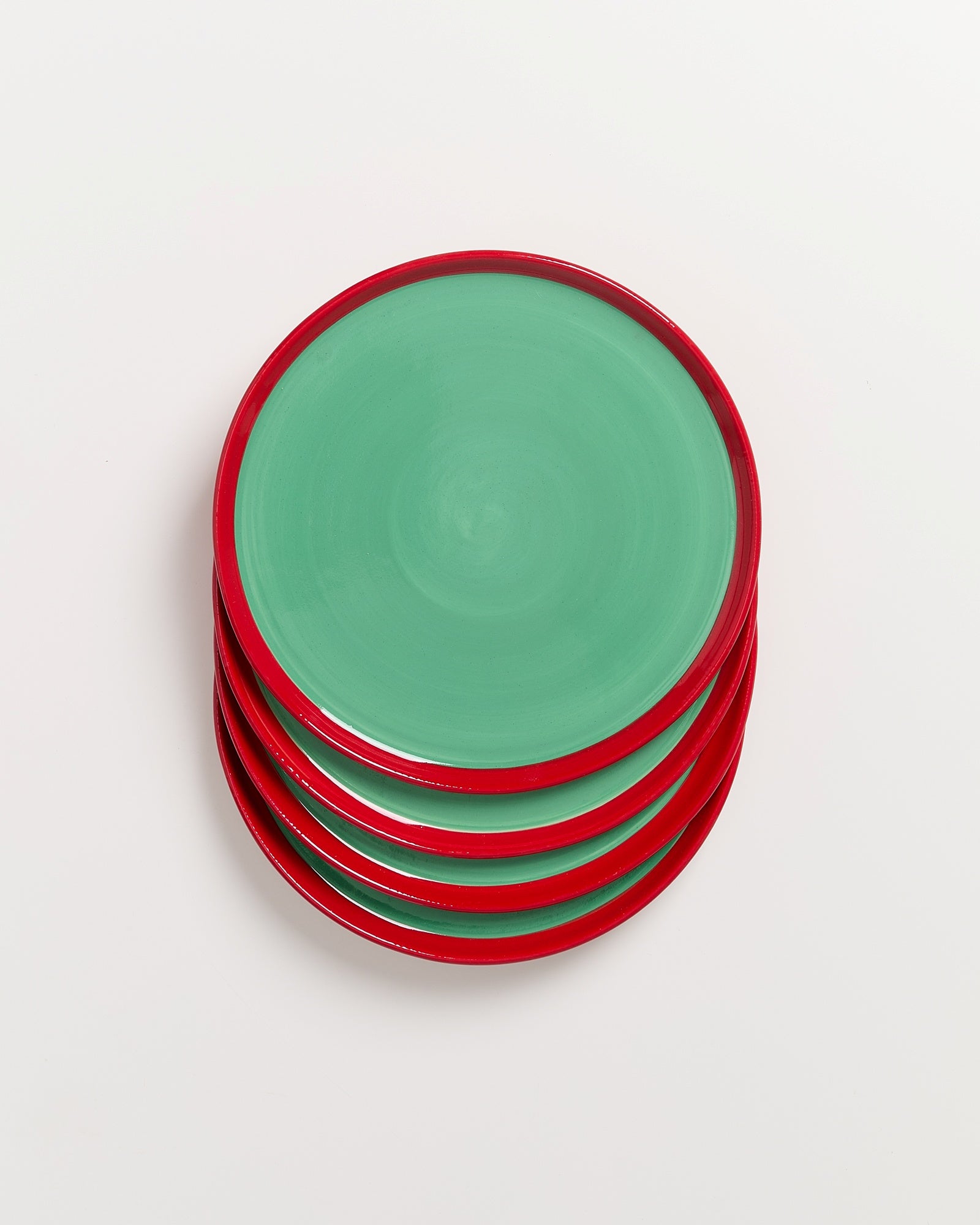 Ein Stapel von fünf grünen Tellern mit roten Rändern auf weißem Hintergrund.