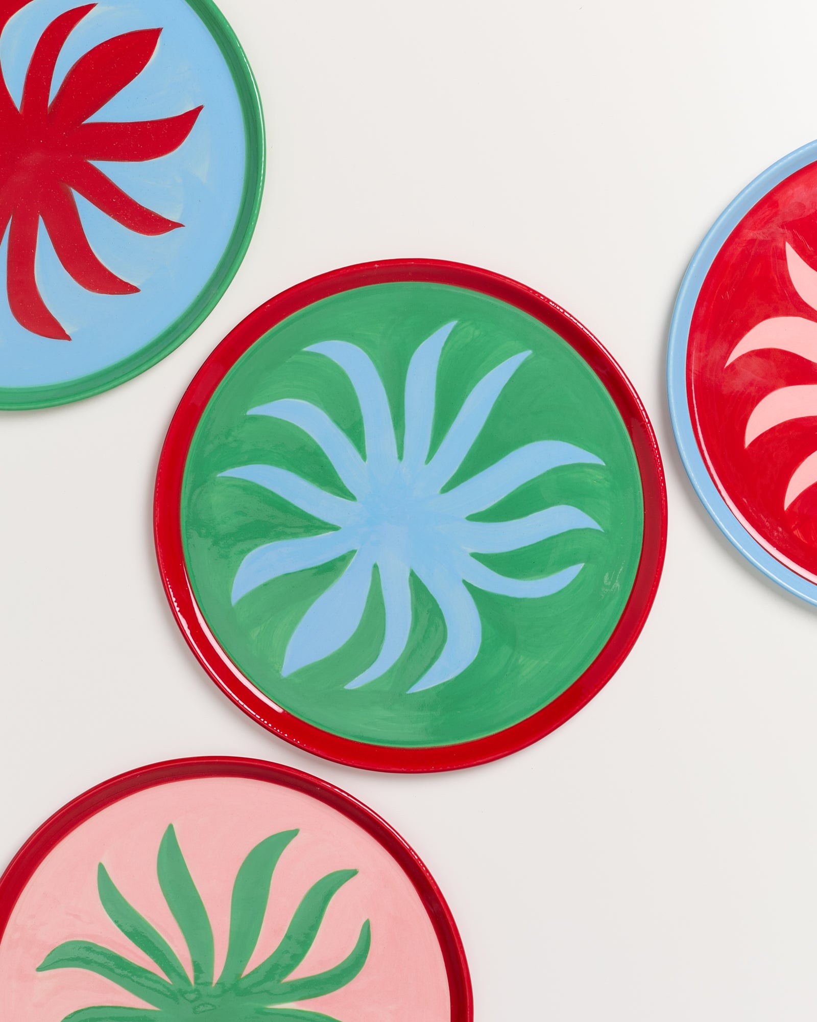 Bunte Teller mit abstrakten, blattähnlichen Mustern auf farbigen Hintergründen, übereinandergelegt auf weißem Hintergrund.