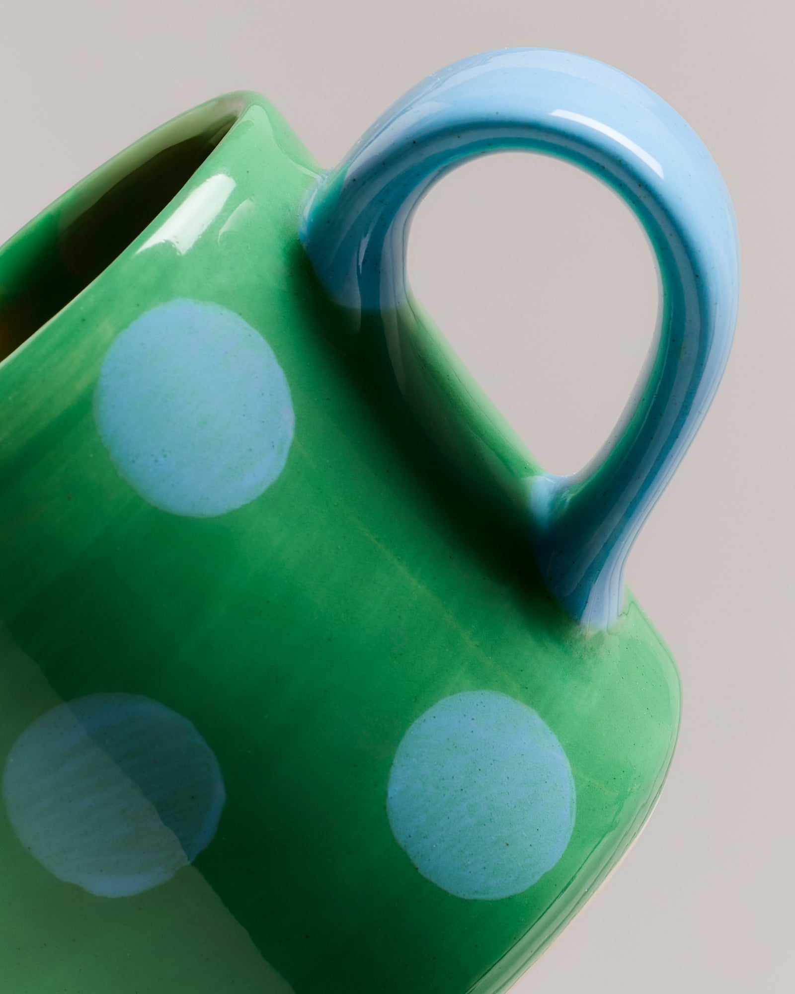Grüne Tasse mit blauen Punkten und blauen Henkel, in Nahaufnahme vor grauem Hintergrund.